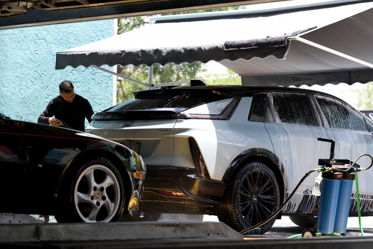 Black sports car parked under a metal staircase in a dim garage, front view.