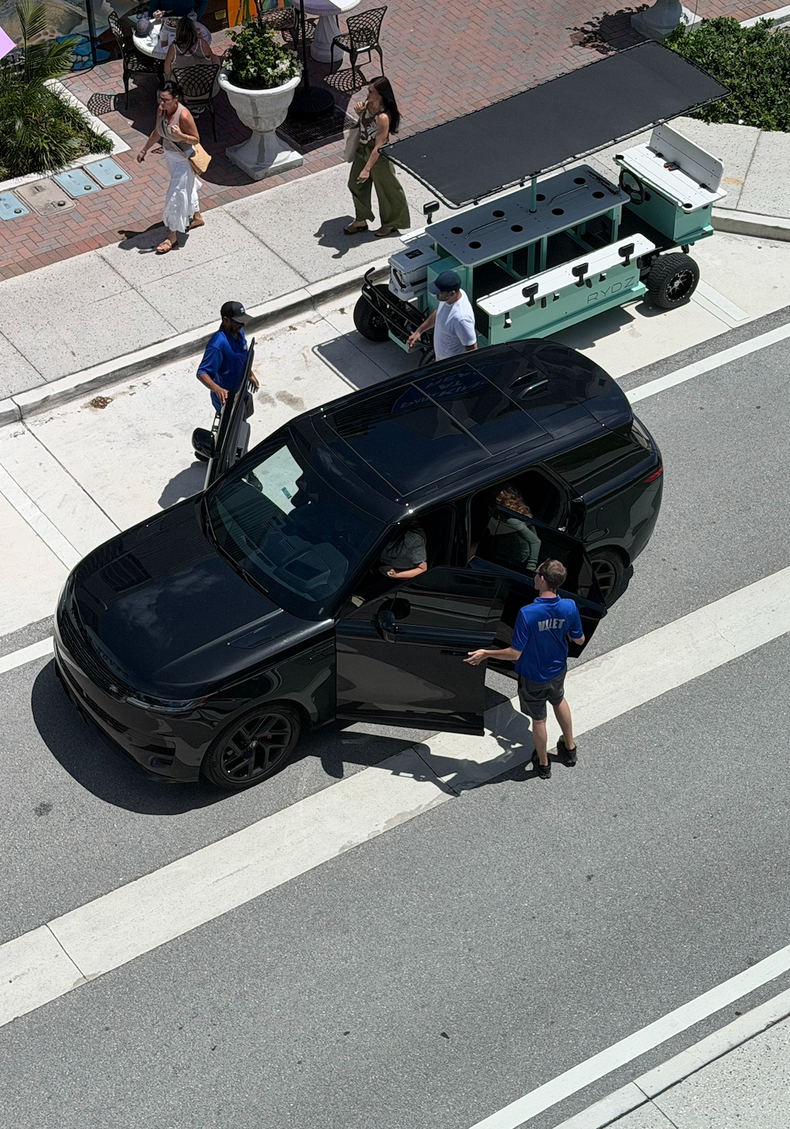 Police officers stand by a black SUV on a city street beside a green utility vehicle.