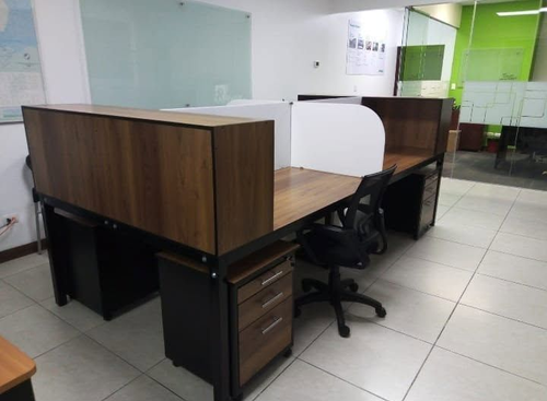 Espacio de oficina moderno con escritorios de madera, cajoneras negras, sillas y mamparas de cristal sobre suelo de baldosas.