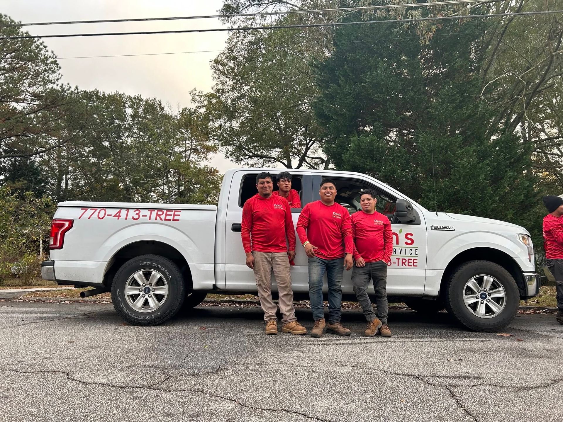 Four workers in red shirts stand beside a white pickup truck on a roadside.