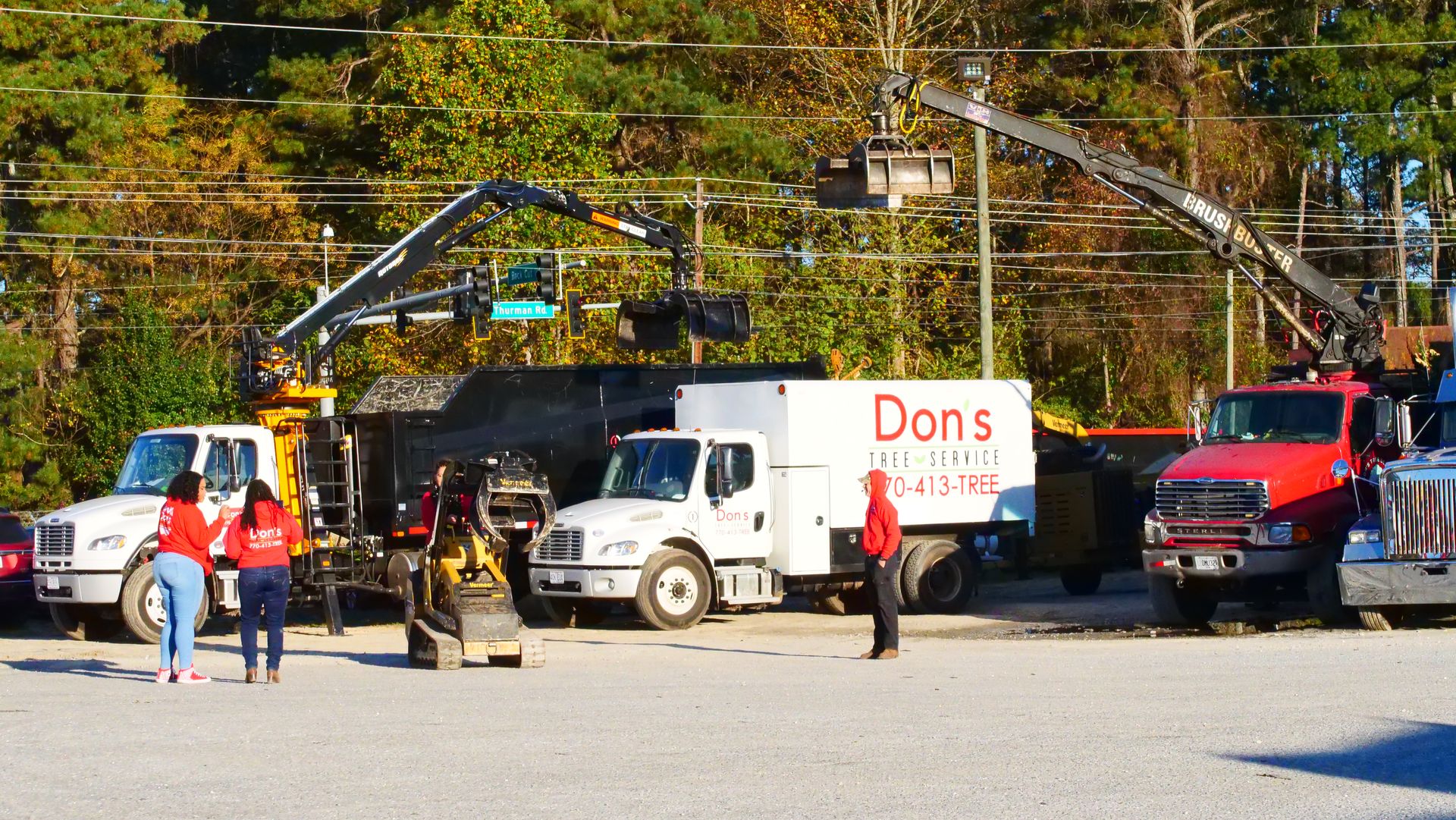 Work trucks and workers parked along a street under trees, with a white truck labeled “Don’s” and a red pickup.