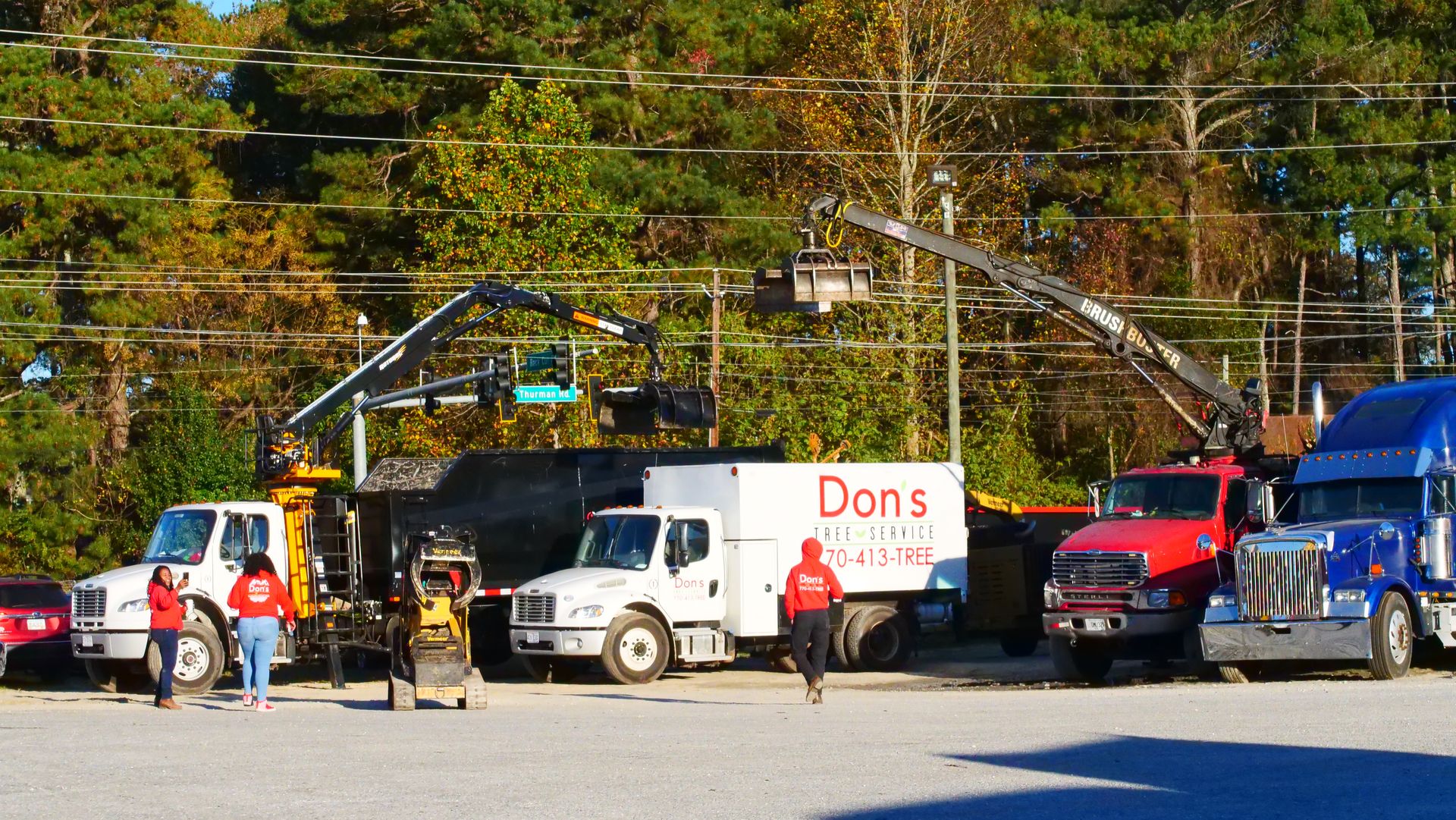 Delivery trucks and workers in a lot, including a white truck labeled “Don’s,” with trees in the background