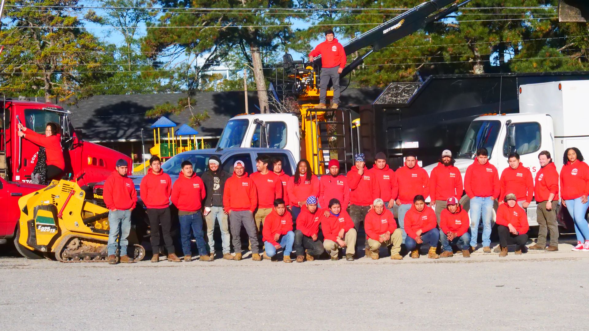 Group of workers in red jackets posing with construction trucks and equipment outdoors