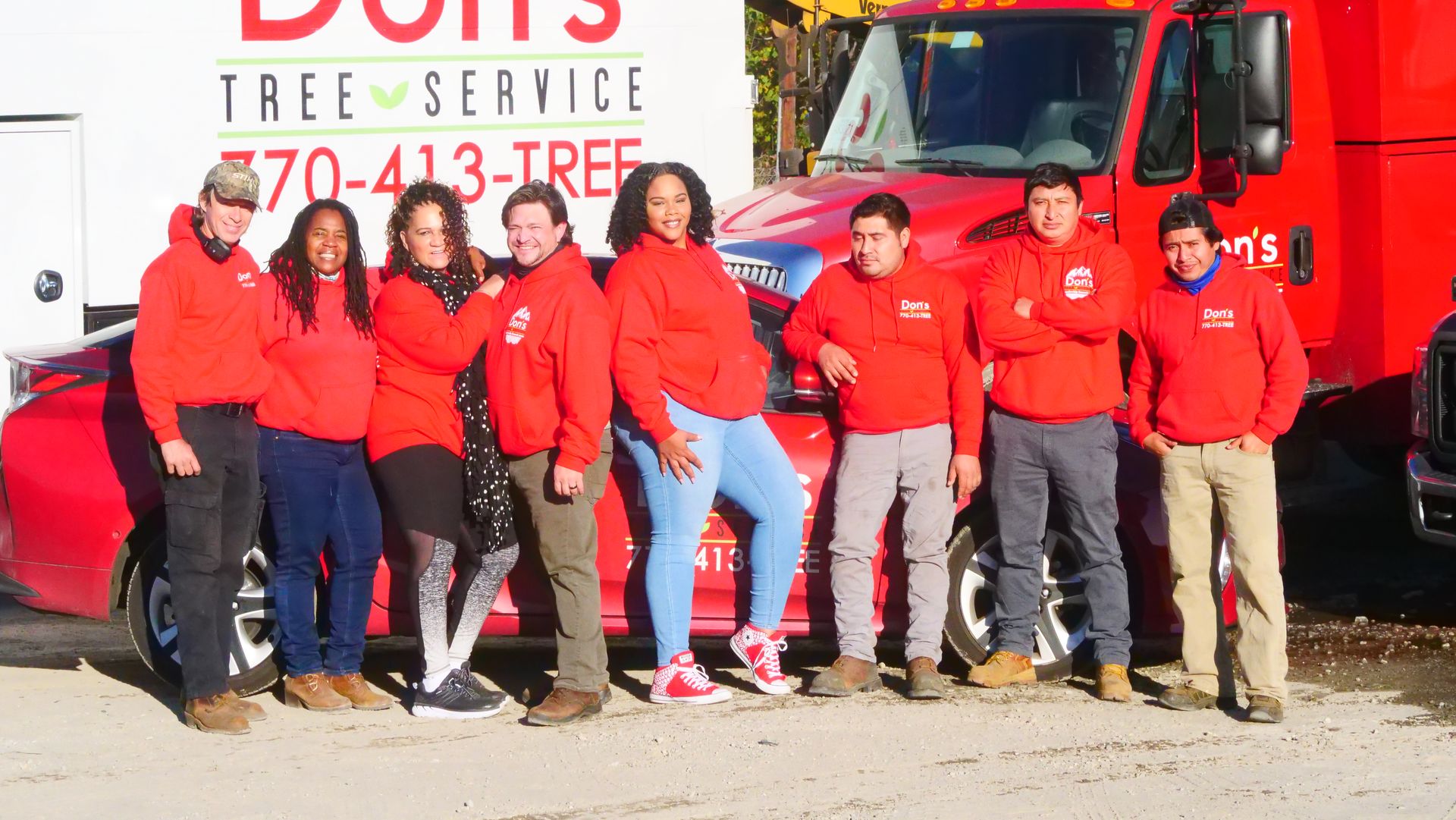 Red-uniformed tree service crew posing in front of a red truck outdoors