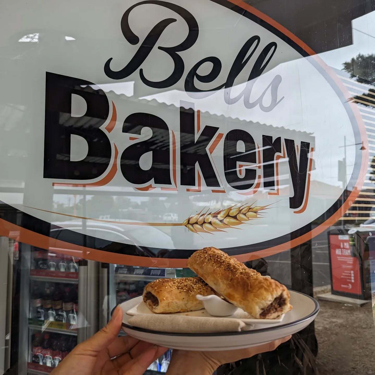 Hand holding a plate of pastries in front of a Bell’s Bakery storefront window