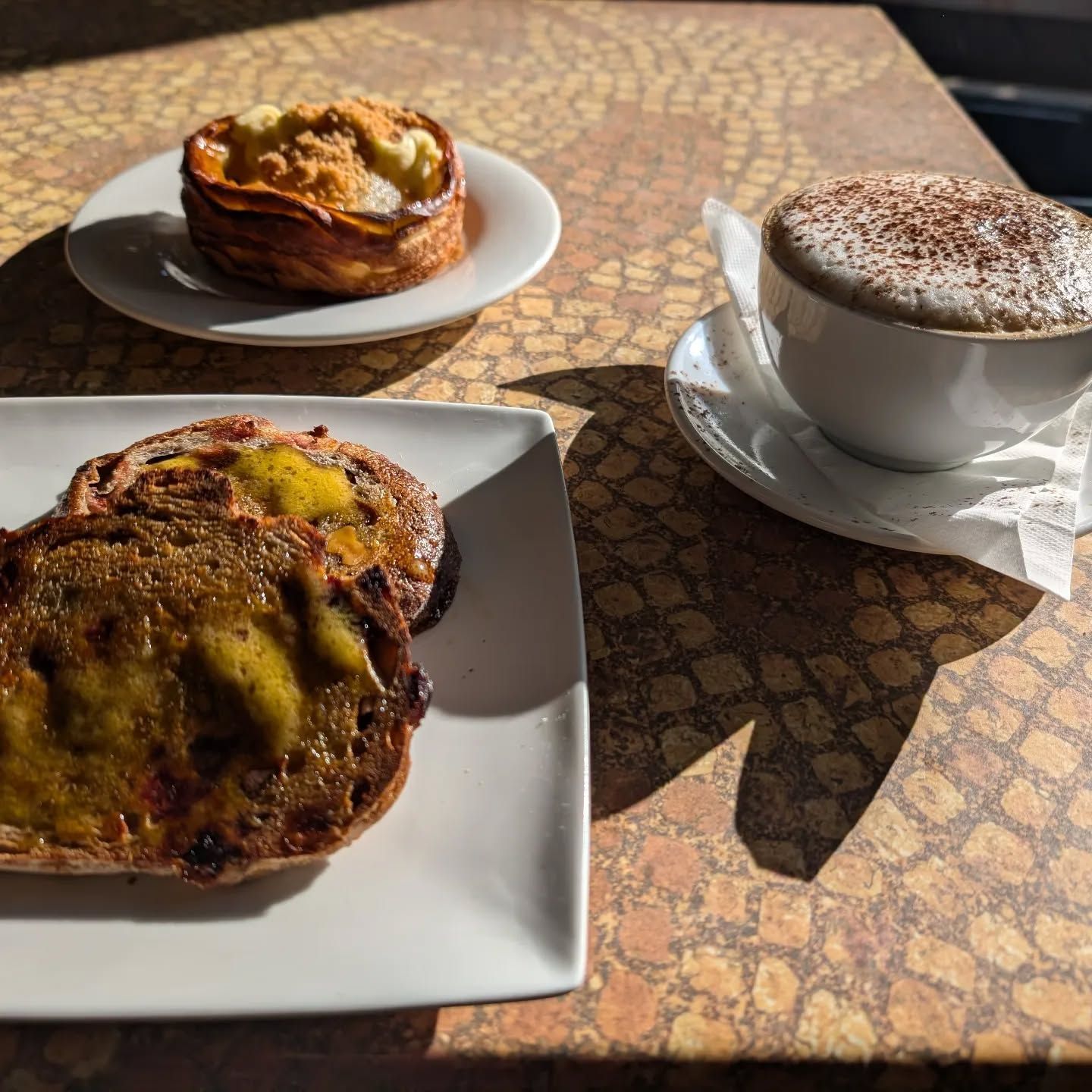 Pastries and a cappuccino on a sunlit café table
