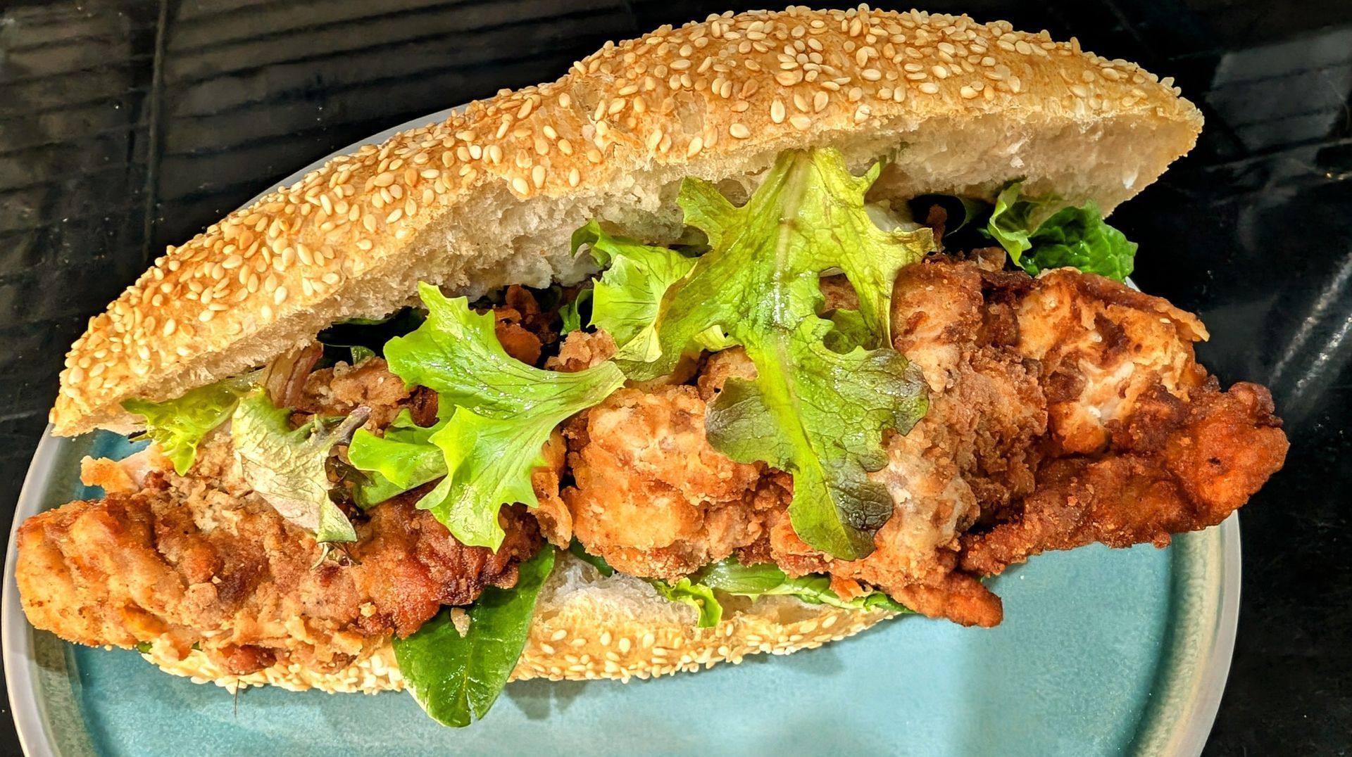 Sesame seed sandwich with fried chicken and lettuce on a plate