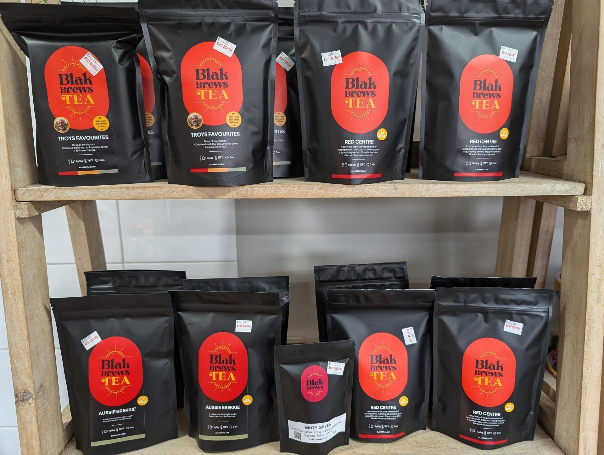 Black coffee bags displayed on wooden shelves, with orange labels and one smaller bag in front