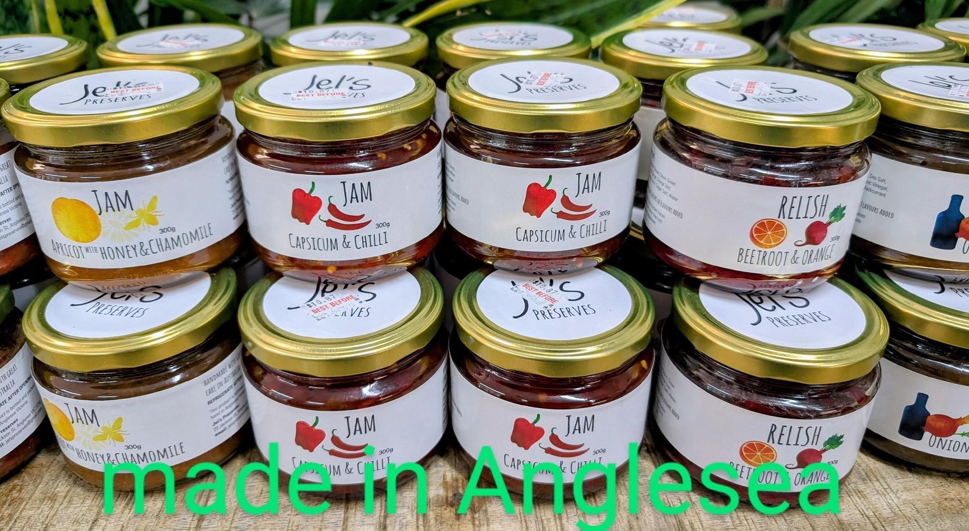 Rows of small glass jam jars with gold lids and fruit labels, overlaid with “made in Anglesea” text