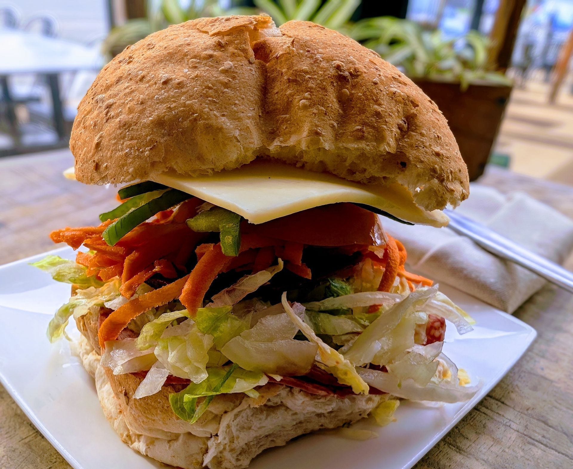 Close-up of a large vegetable sandwich on a white plate, with lettuce, tomato, and cheese on a table.