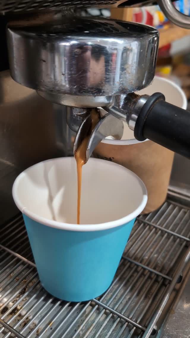 Espresso pouring from a machine into a blue paper cup on a drip tray
