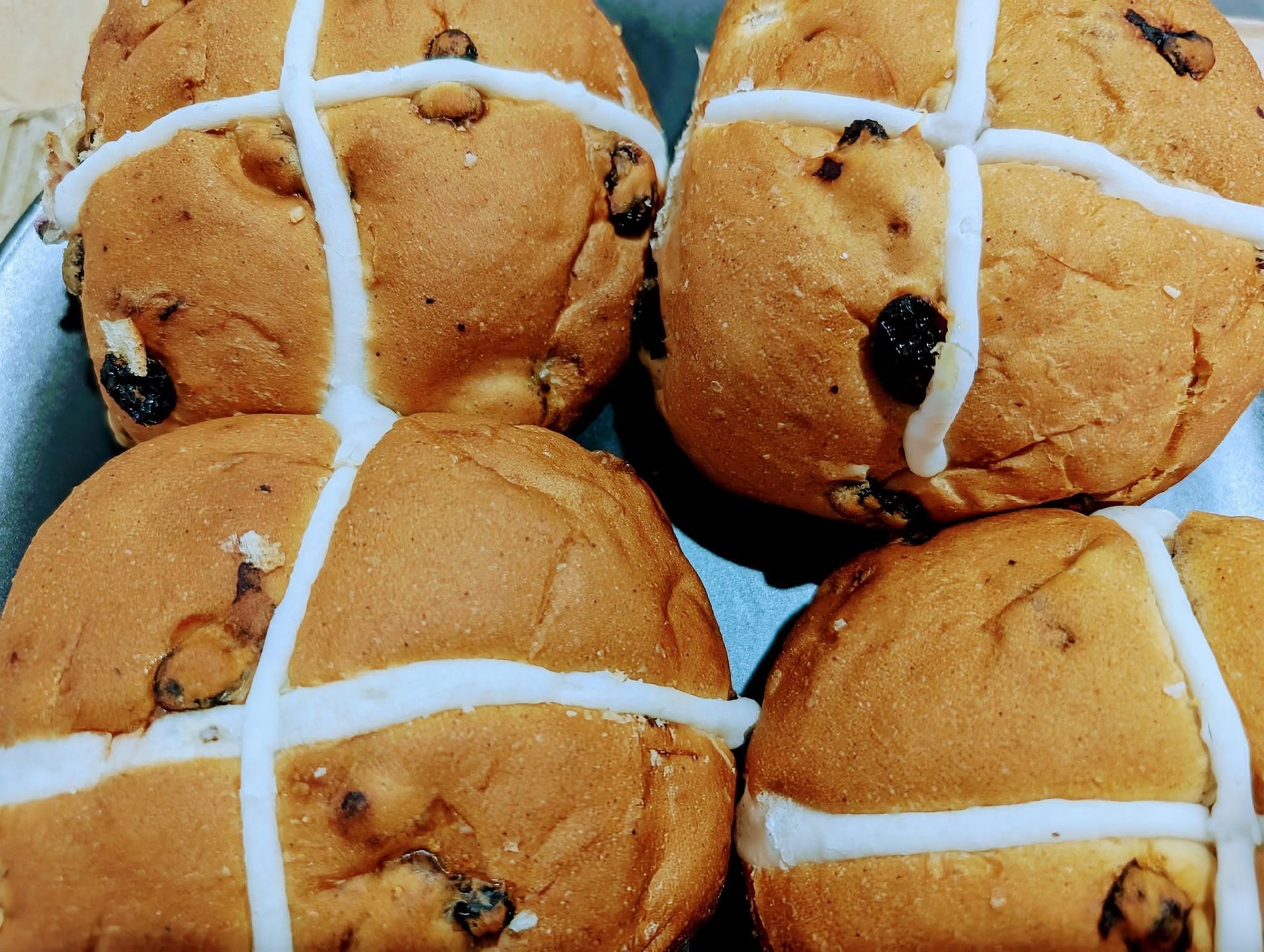 Four hot cross buns with white icing crosses close together on a tray
