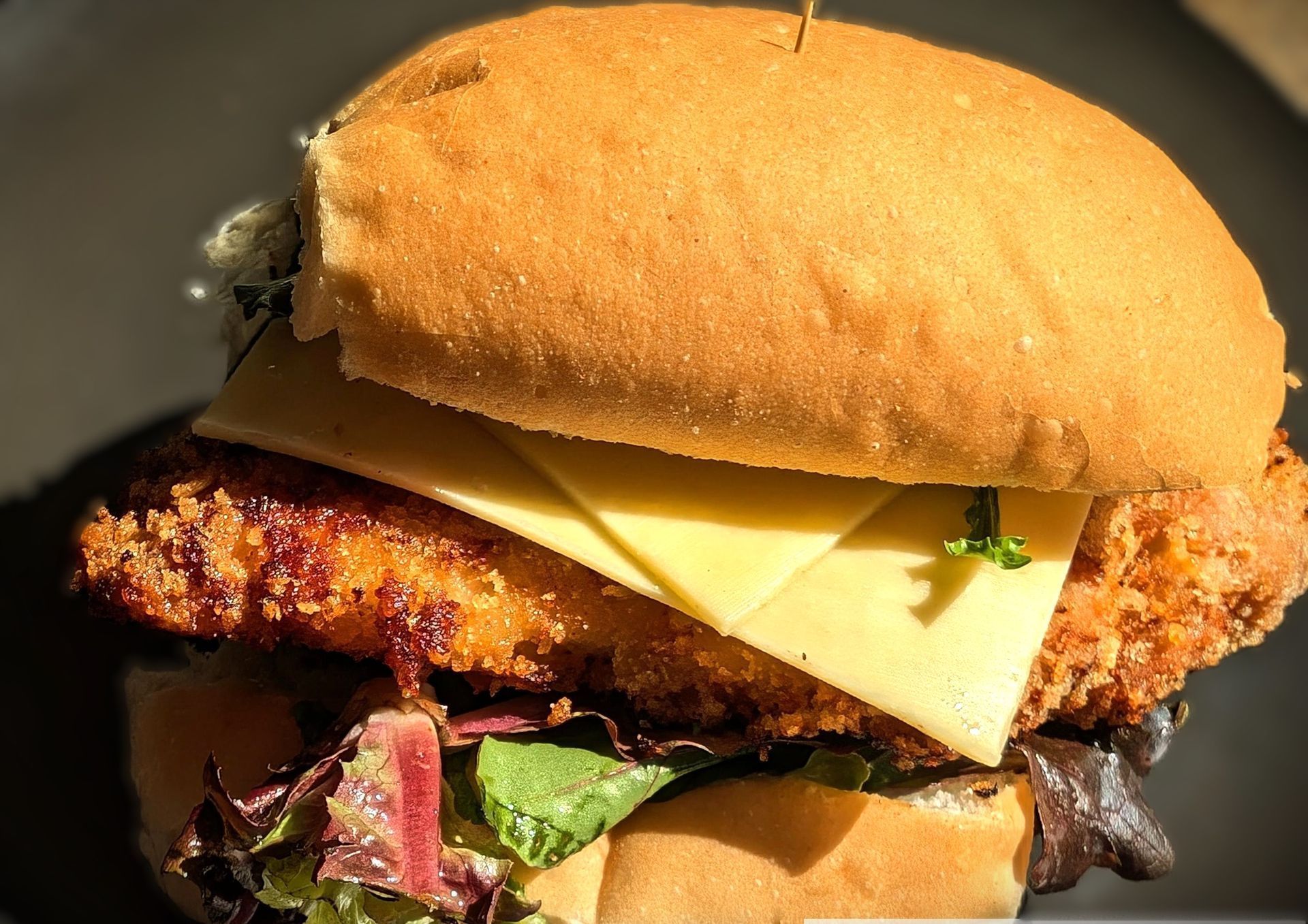 Close-up of a sandwich with a bun, cheese, crispy fried filling, and lettuce on a dark background