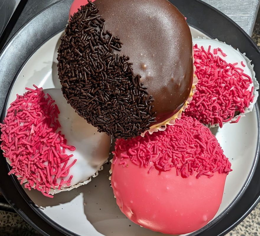 Three frosted donuts on a plate, topped with pink sprinkles and one with chocolate sprinkles.