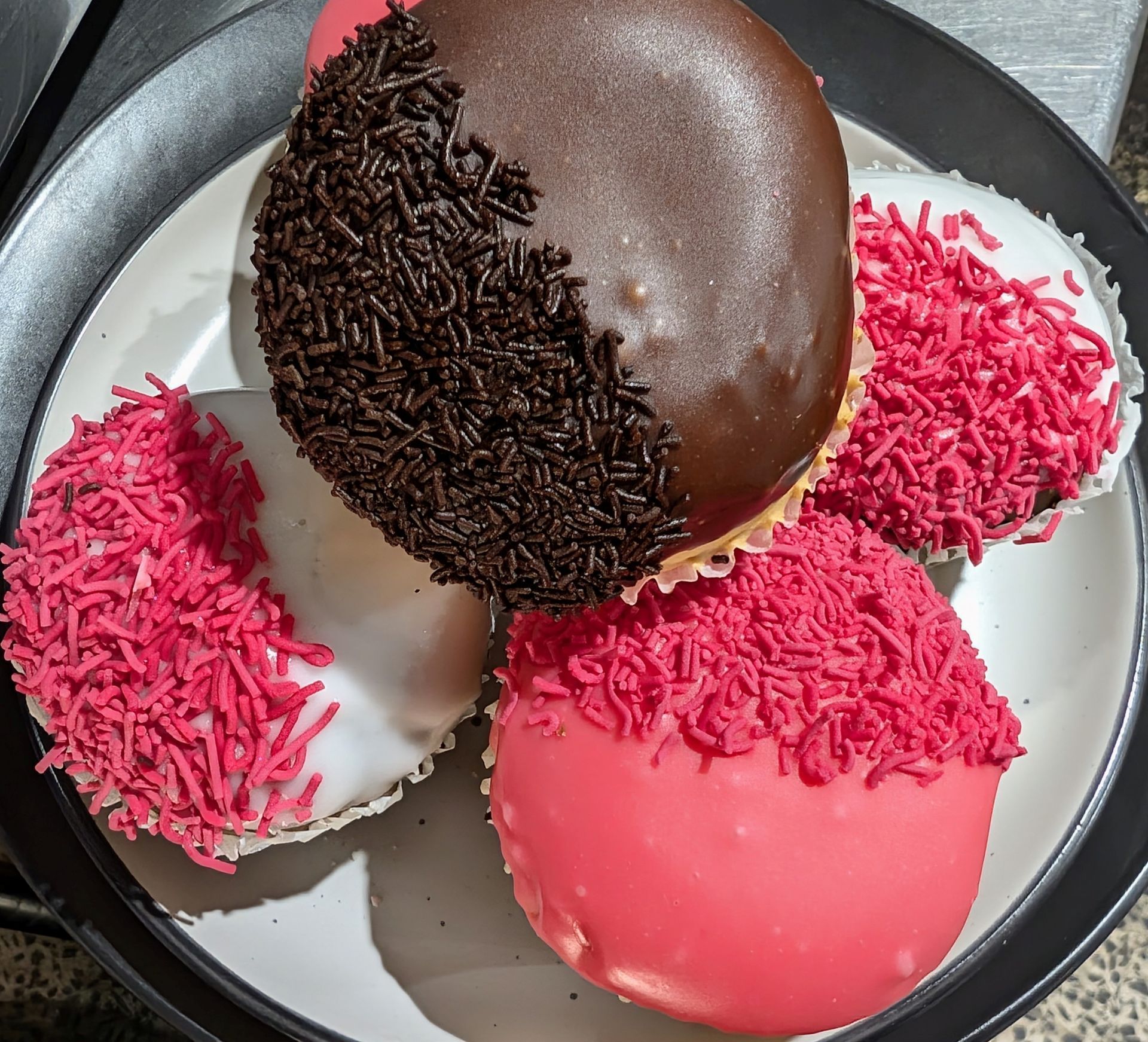 Assorted frosted donuts on a tray, topped with pink and chocolate sprinkles.