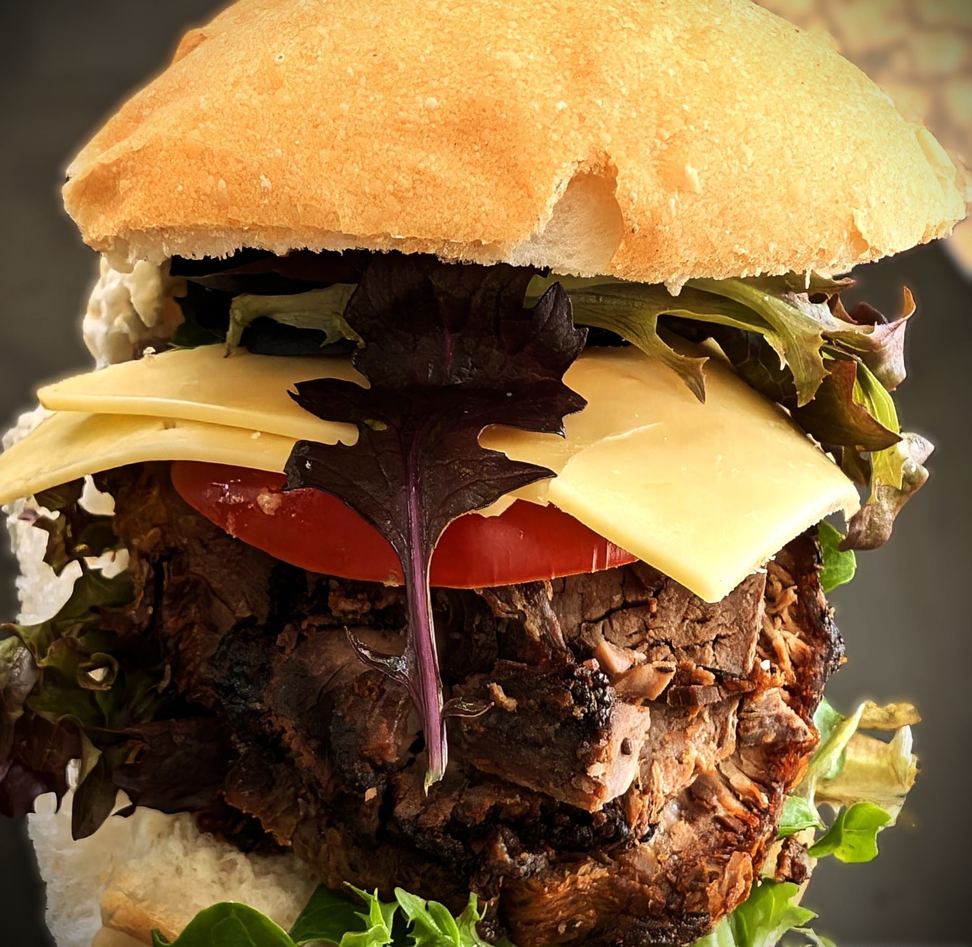 Close-up of a burger with cheese, tomato, lettuce, and a bun.