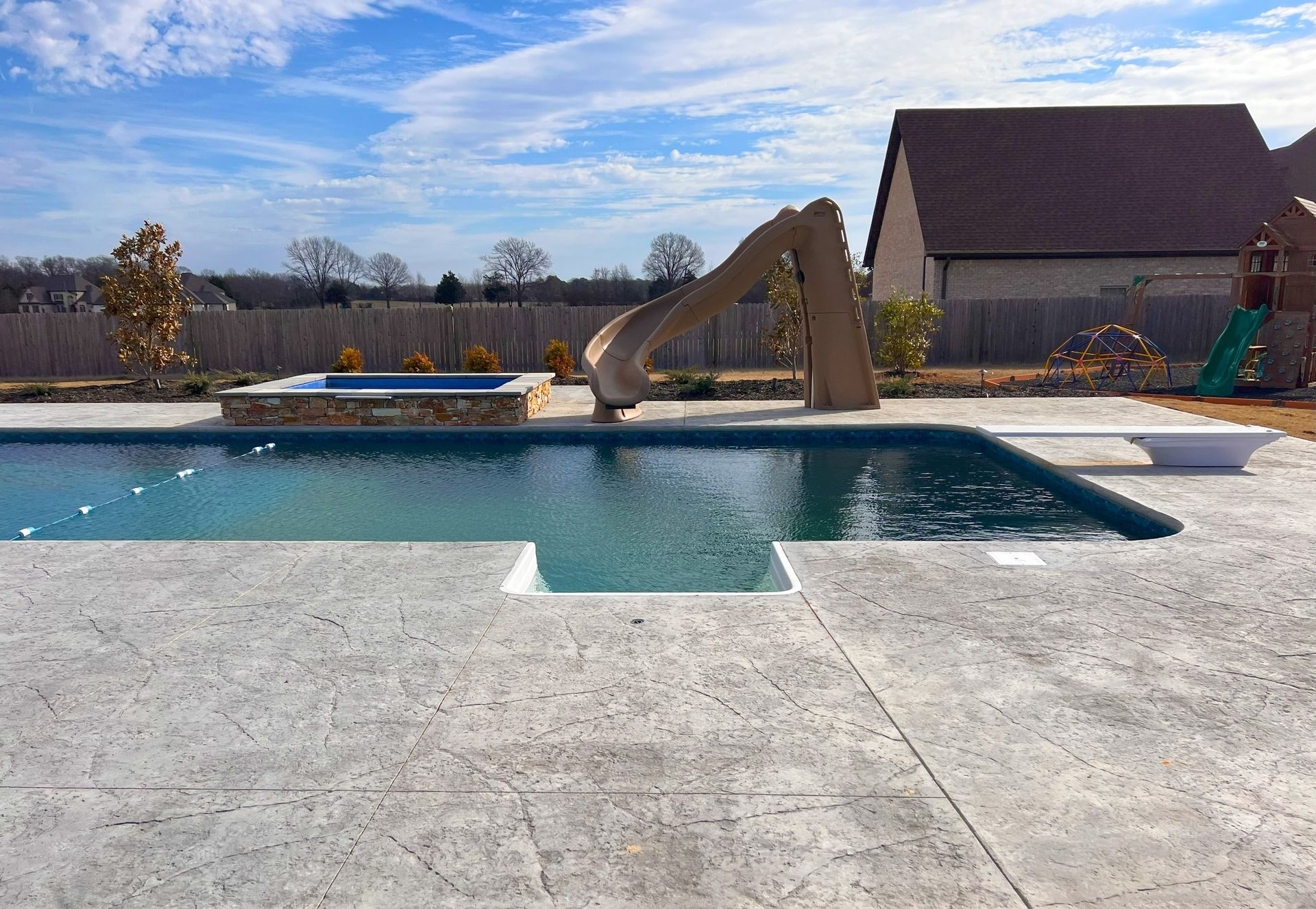 Outdoor pool with tan deck, curved slide, and a building under a clear blue sky