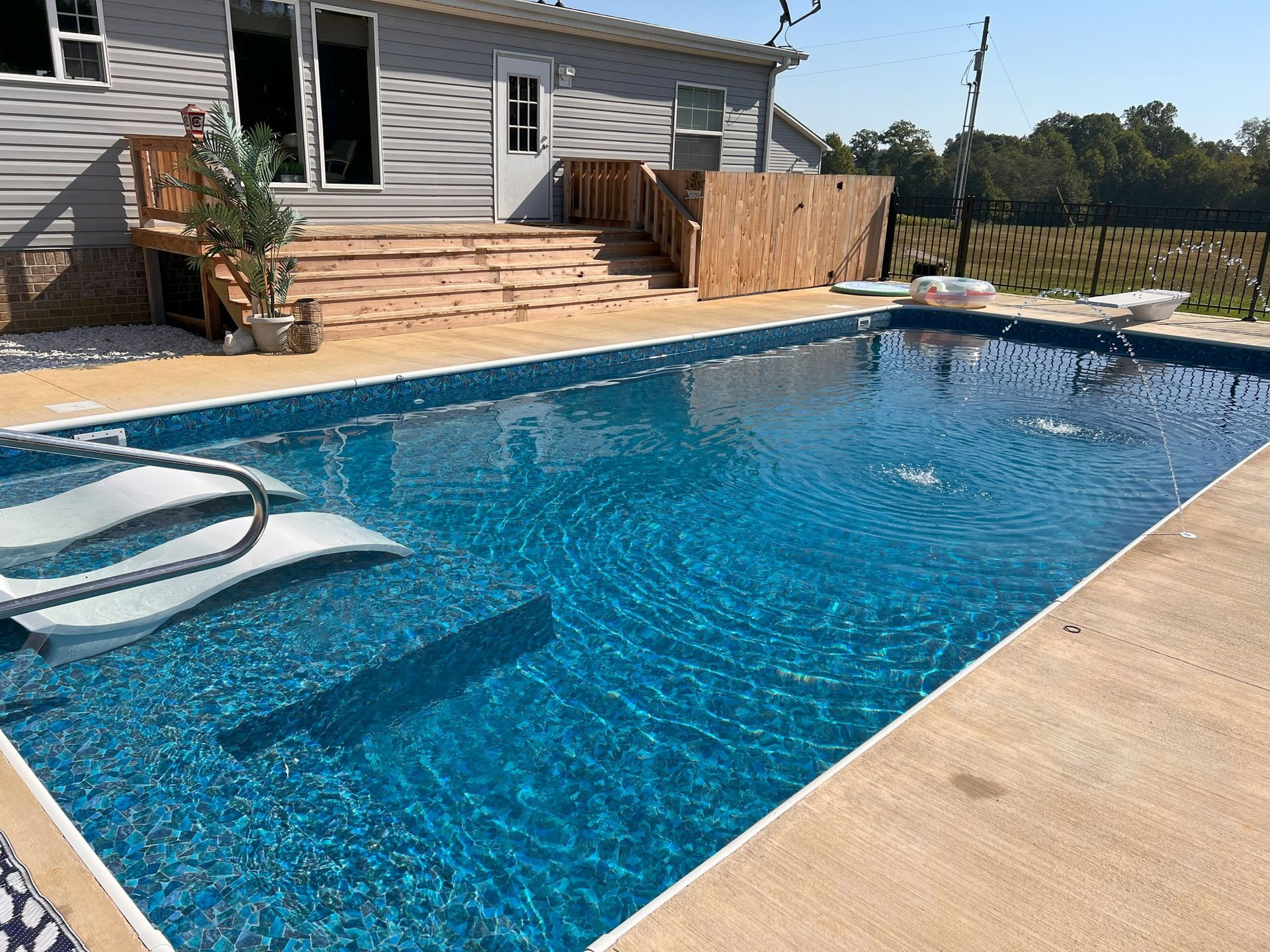 Backyard pool with blue water, patio deck, stairs, and a house in the background