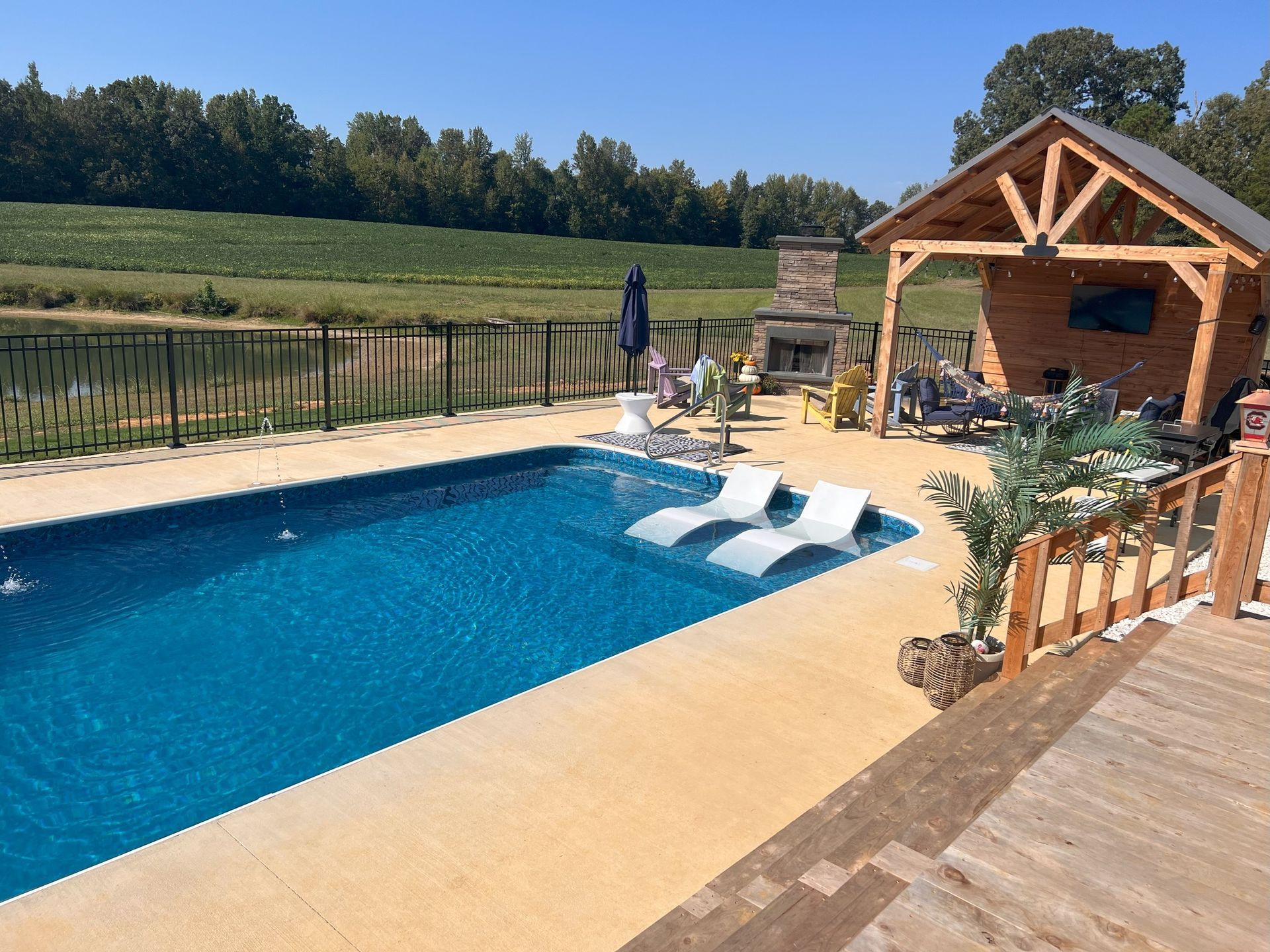 Backyard pool with lounge chairs, wooden cabana, and a rural field beyond the fence