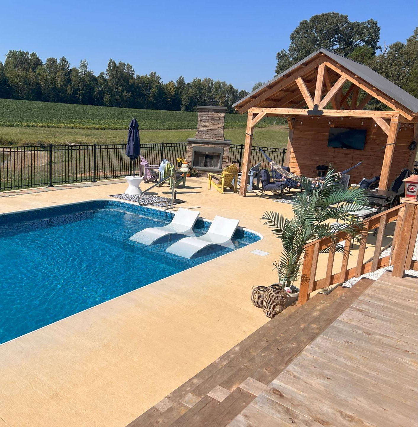 Backyard pool with white loungers, wooden pergola, and open countryside beyond