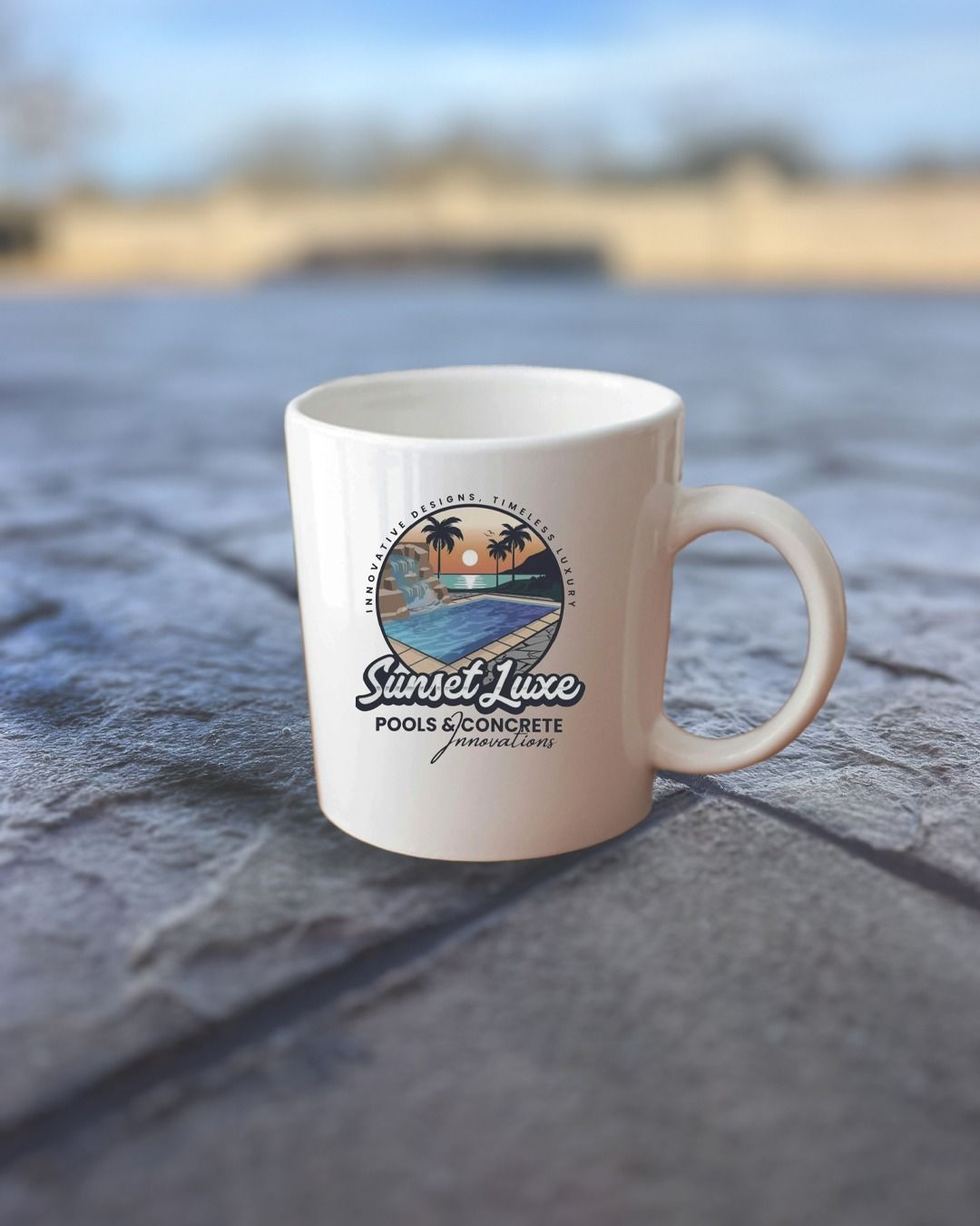 White mug with Sunset Juice logo on a stone surface by a blurred waterfront background