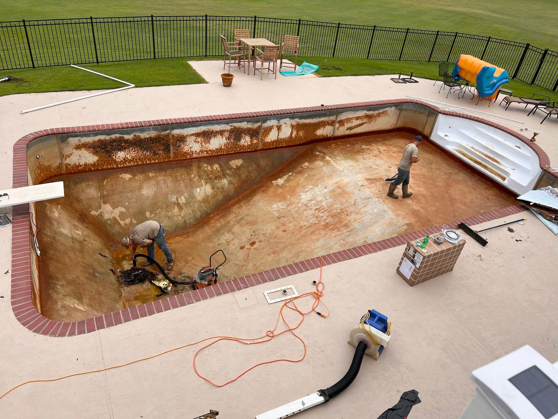 Workers cleaning an empty in-ground pool with hoses and equipment on the deck