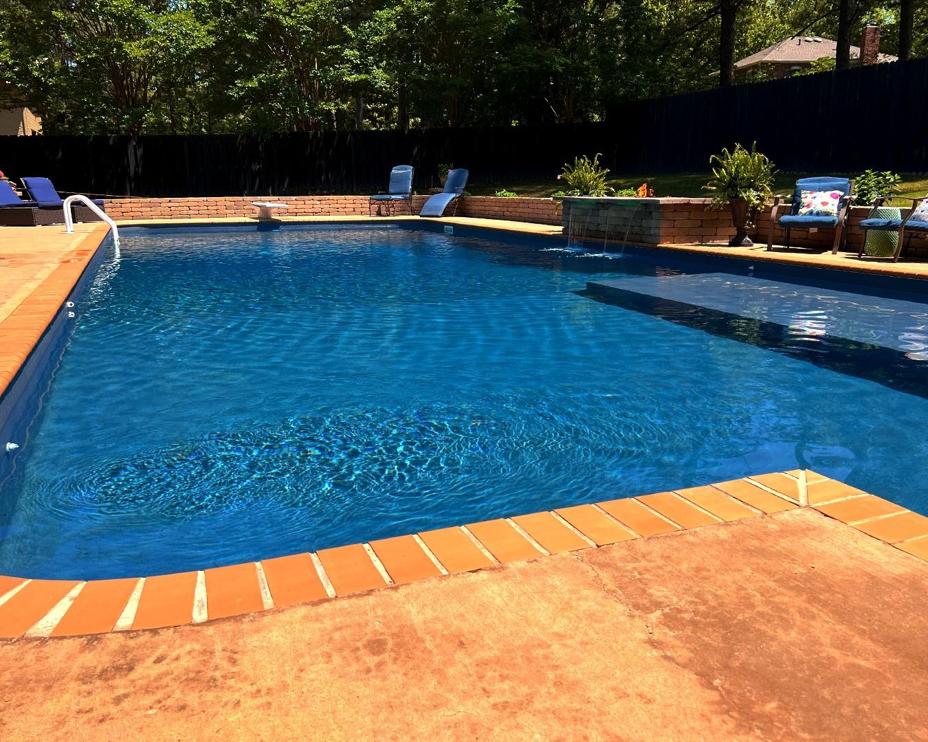 Outdoor swimming pool with blue water, orange tile border, and lounge chairs by greenery