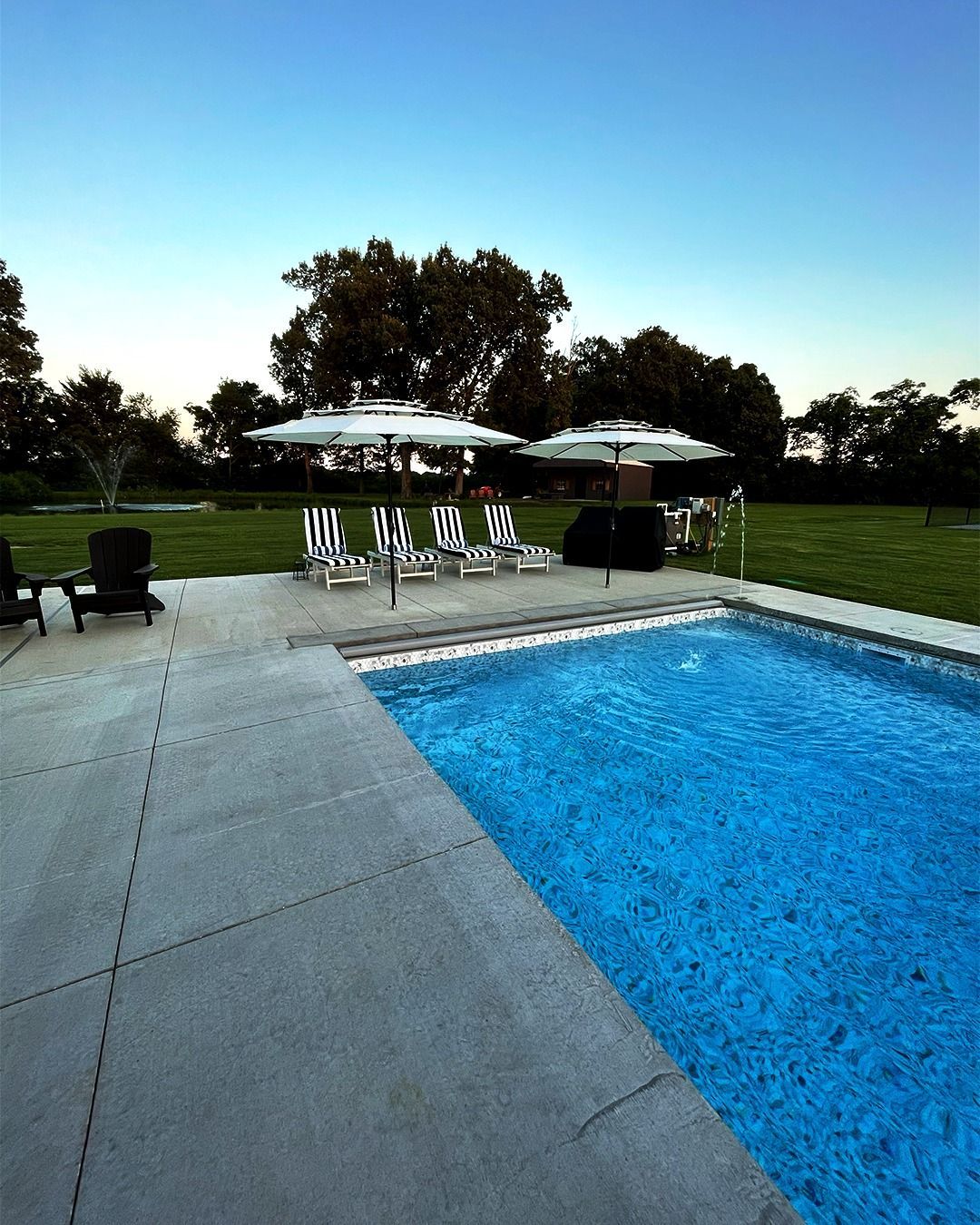 Backyard pool with lounge chairs, covered seating, and a grassy lawn at dusk