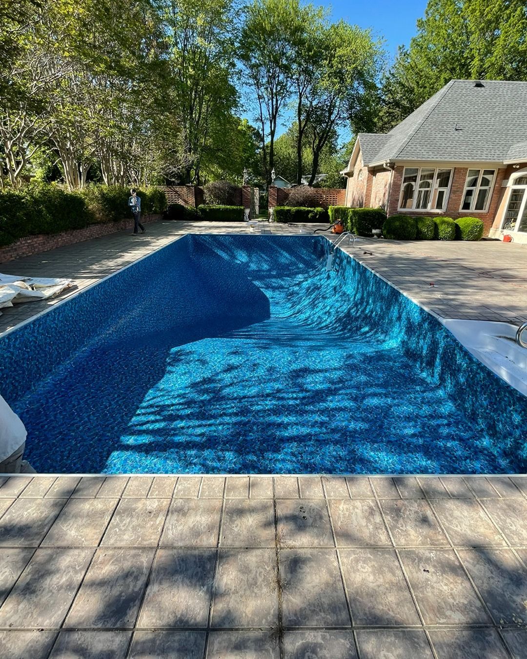Backyard swimming pool with blue cover, surrounded by patio and trees beside a house