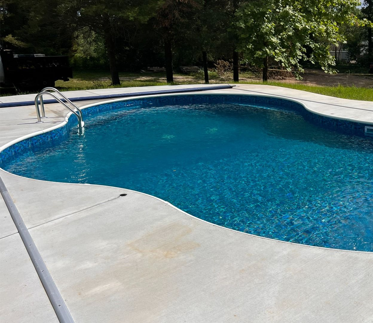 Blue swimming pool with curved concrete deck and trees in the background