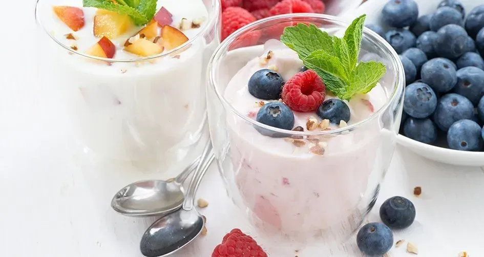 Three glasses of yogurt with raspberries , blueberries and peach.