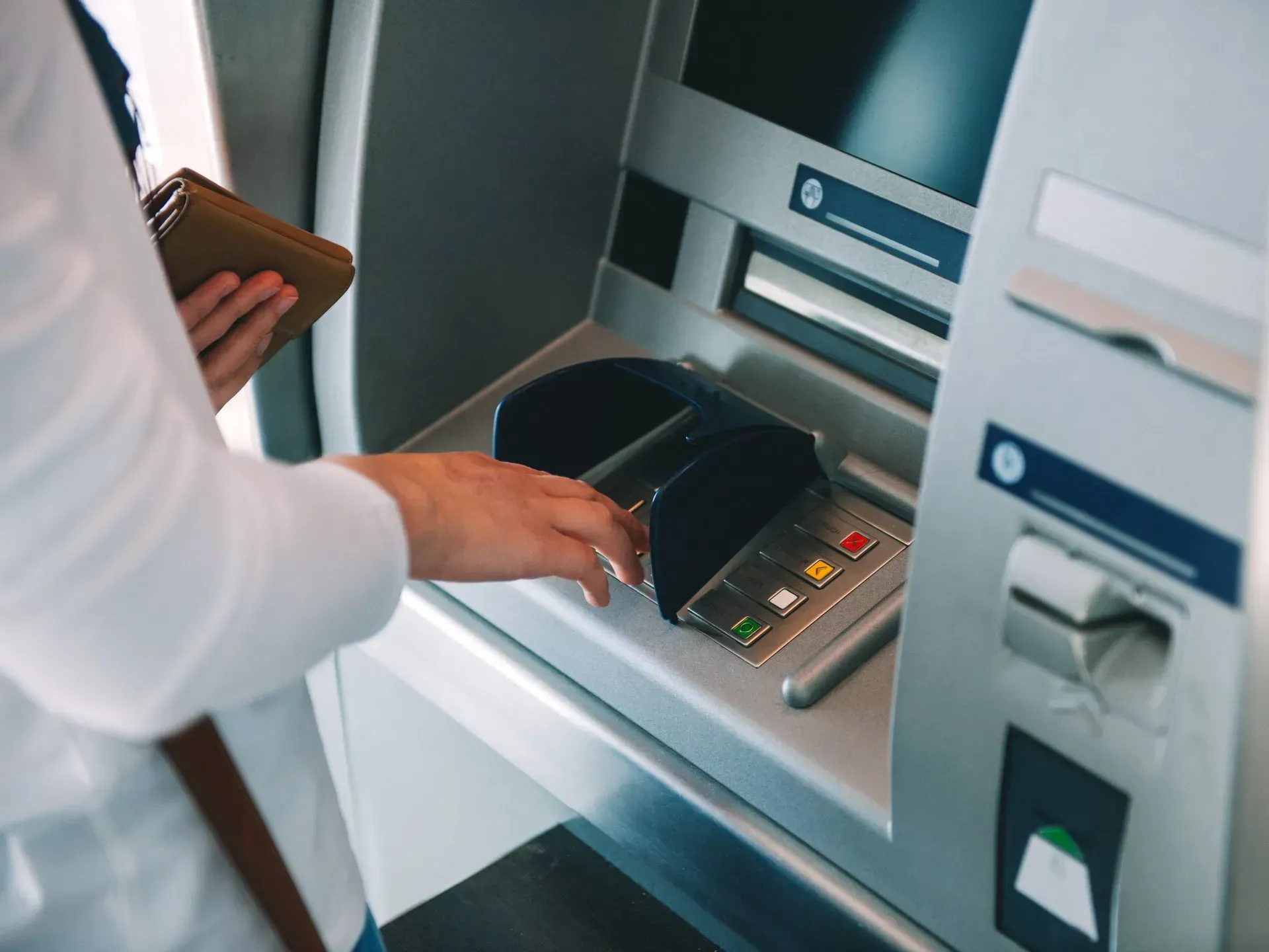 A woman is using an atm machine while holding a wallet.