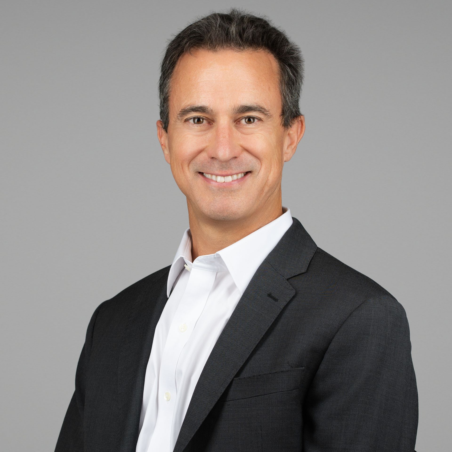 Smiling man in a dark blazer and white shirt against a gray background