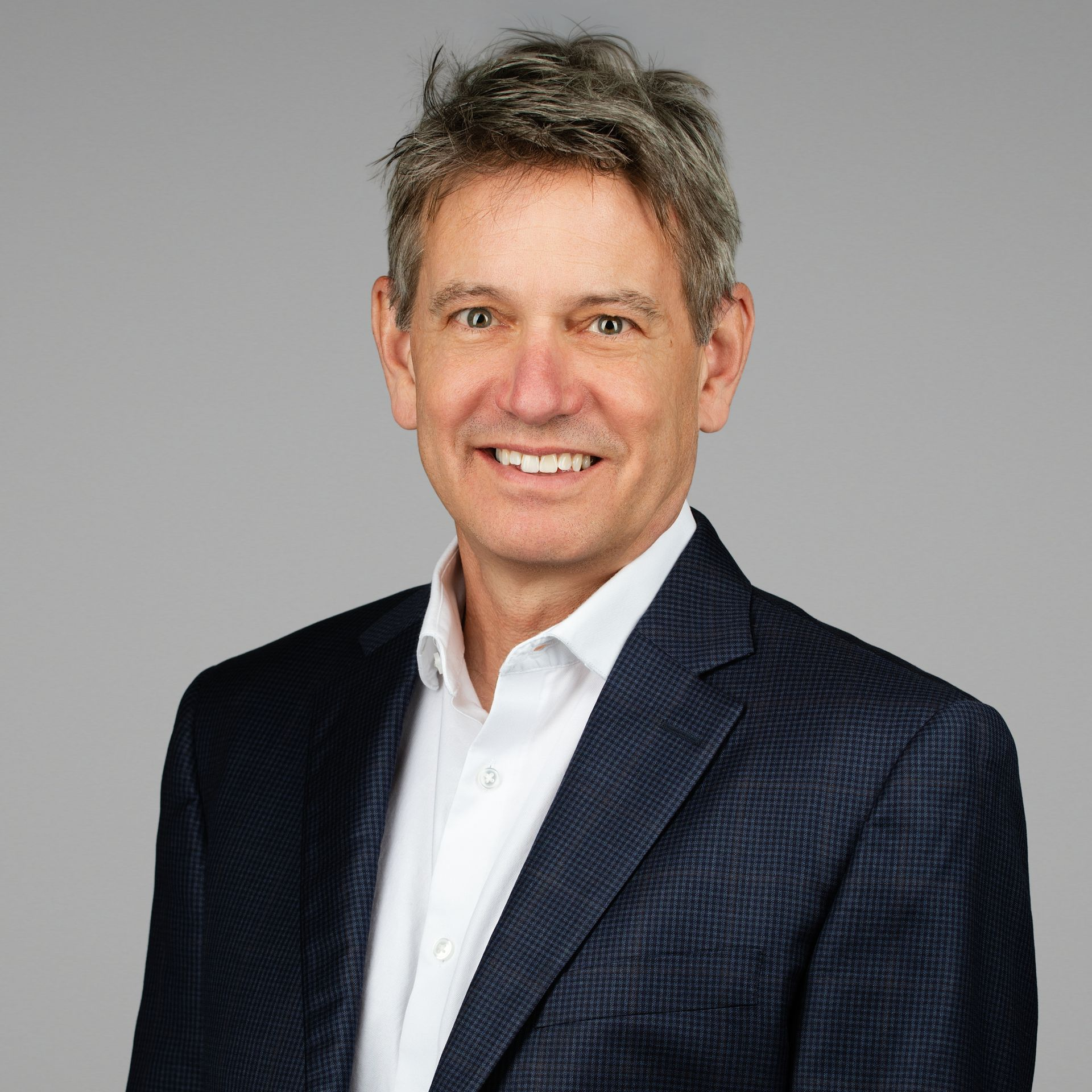 Smiling man in a dark blazer and white shirt against a gray background