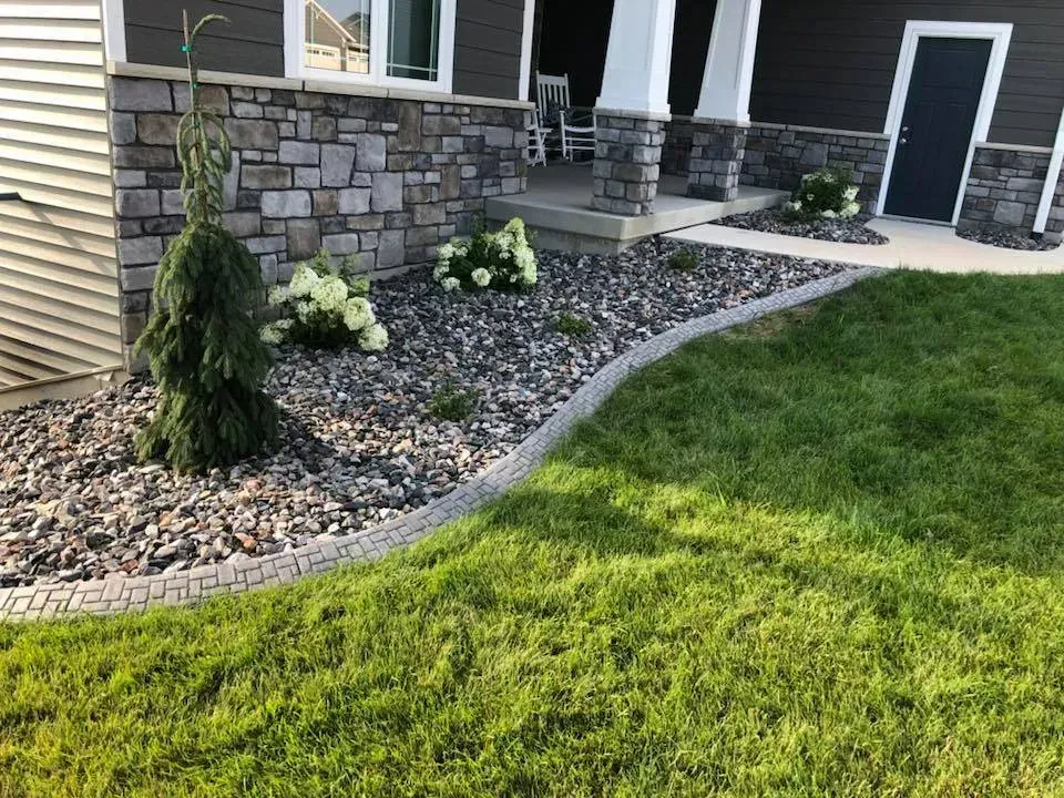 Landscaped front yard with gray stone mulch, white hydrangea shrubs, a tall evergreen, and a curved brick border.