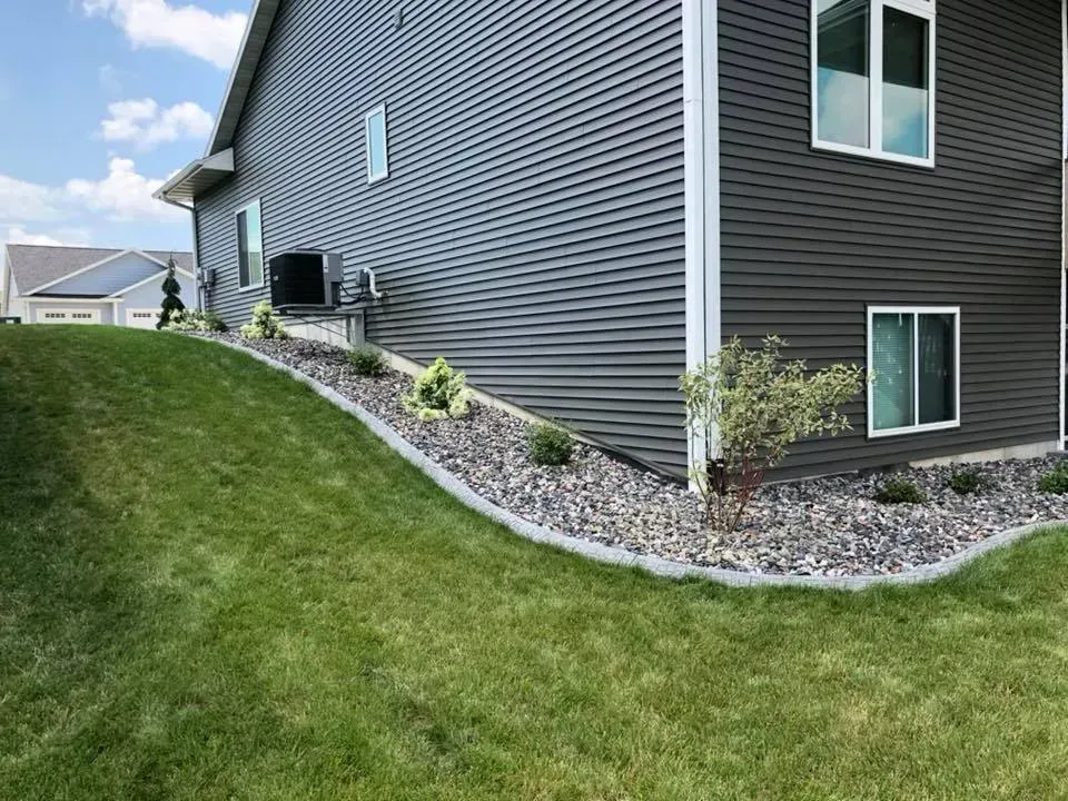 Gray house with dark siding, stone landscaping bed, and sloped green lawn under a sunny, blue sky.