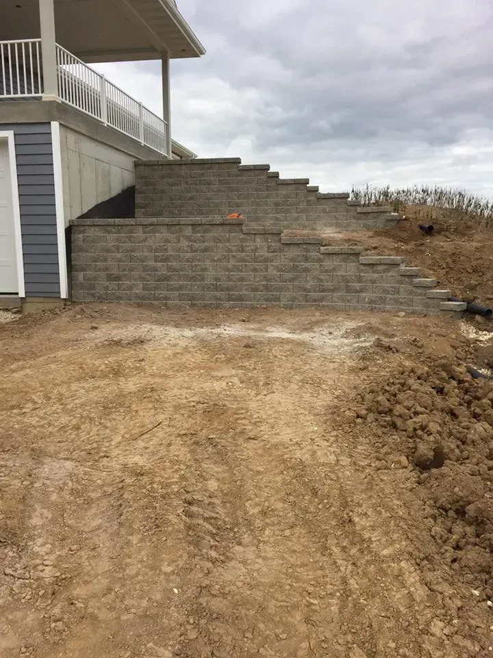A newly constructed tiered stone retaining wall leading up a dirt embankment beside a house with a white deck.