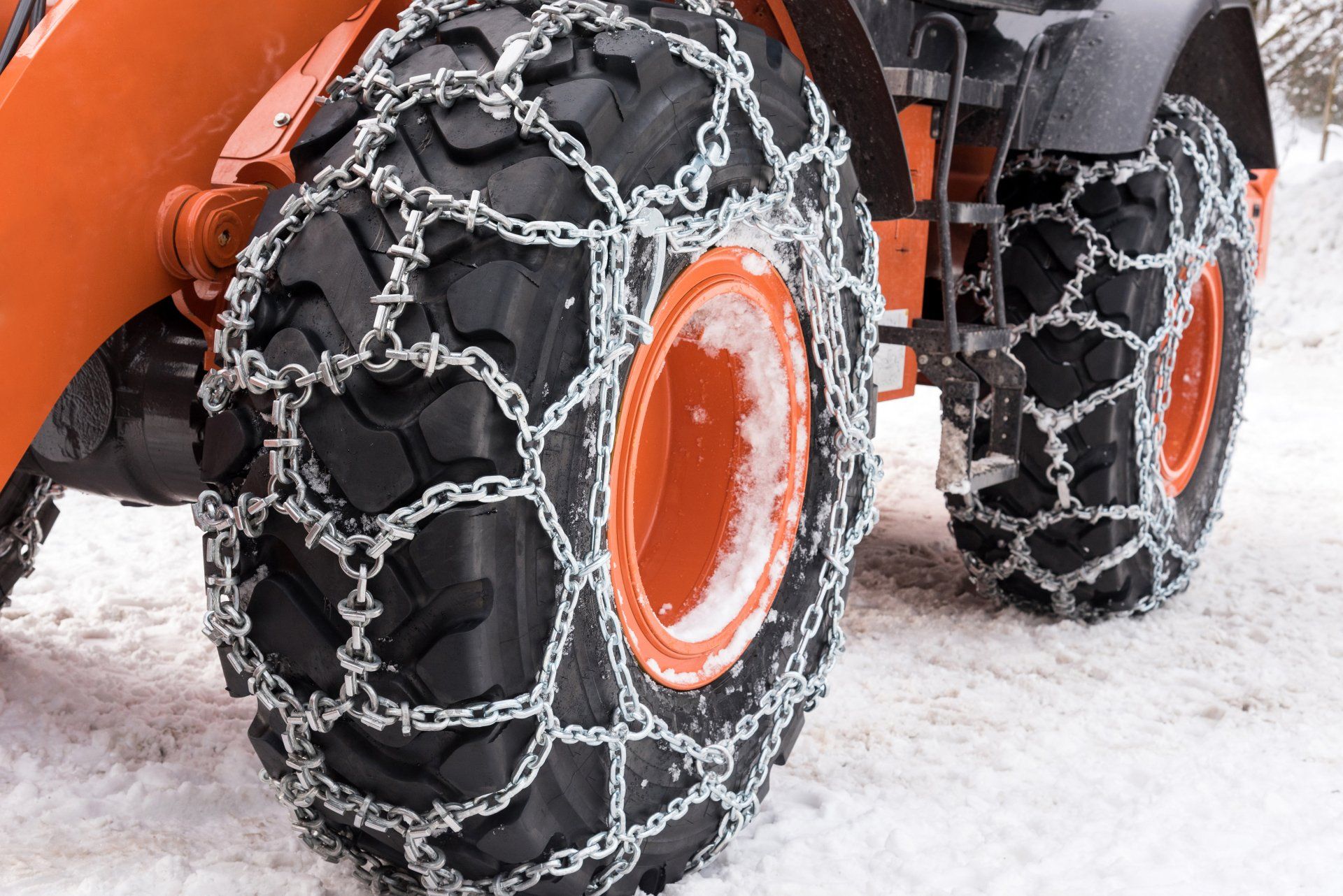 A tractor with chains on the tires is driving through the snow.