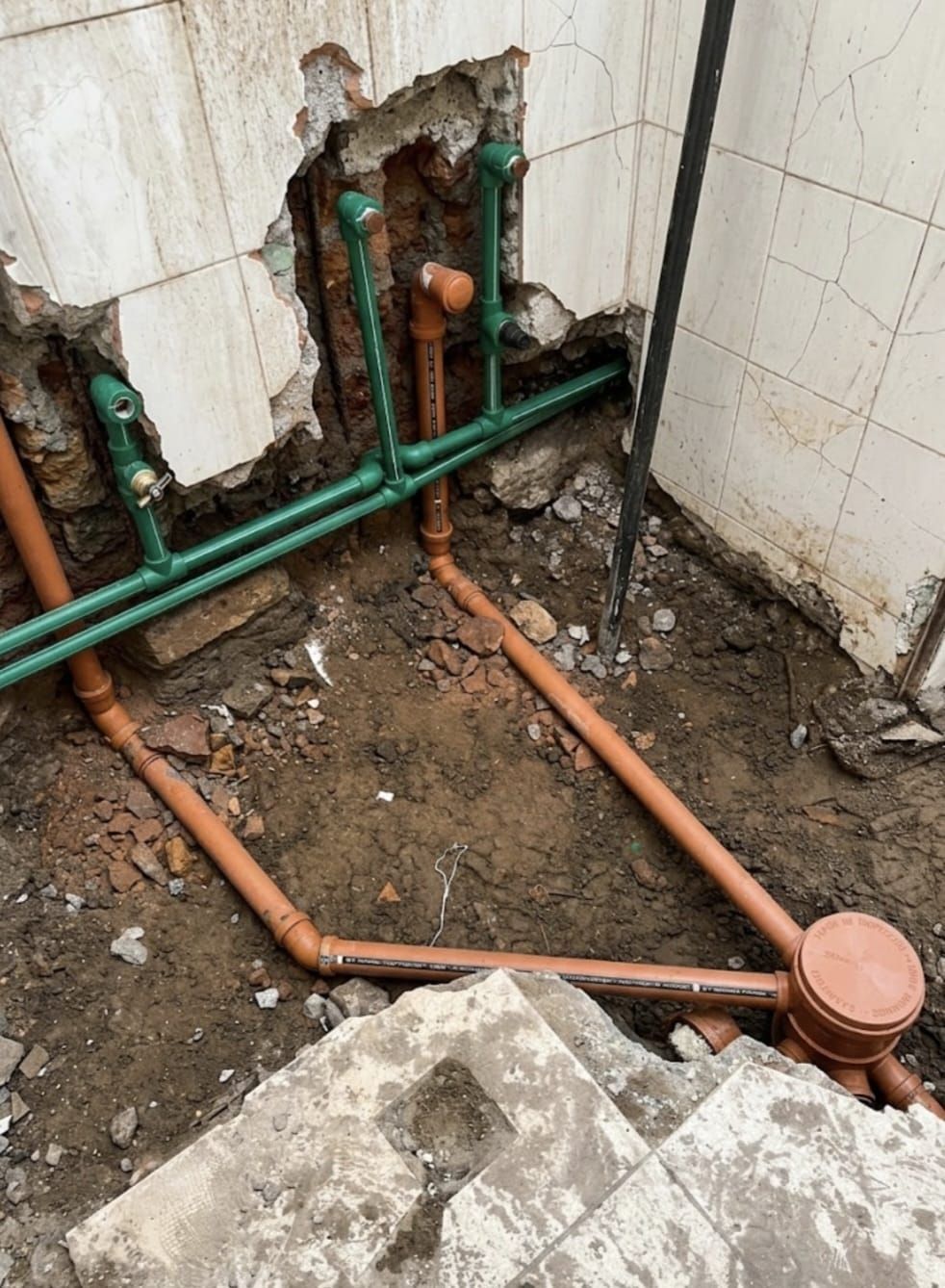 Tuberías de pared a la vista con tuberías verdes y de cobre en un rincón de baño rústico y sin terminar.