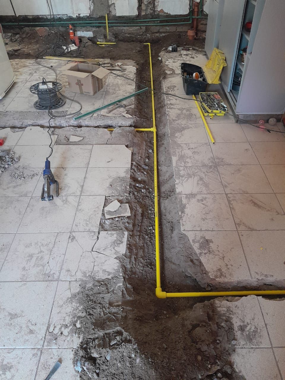 Obra en construcción con suelo al descubierto, tubería de gas amarilla y herramientas en una habitación