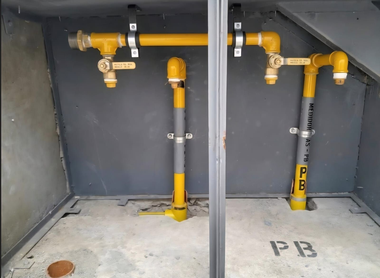 Tuberías y válvulas de gas amarillas montadas en una pared gris de un cuarto de servicio, con la etiqueta P3 en el suelo.