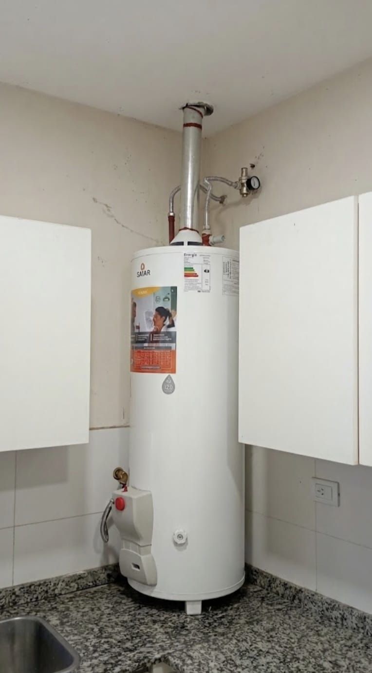 Calentador de agua blanco en un pequeño cuarto de servicio con armarios a ambos lados.