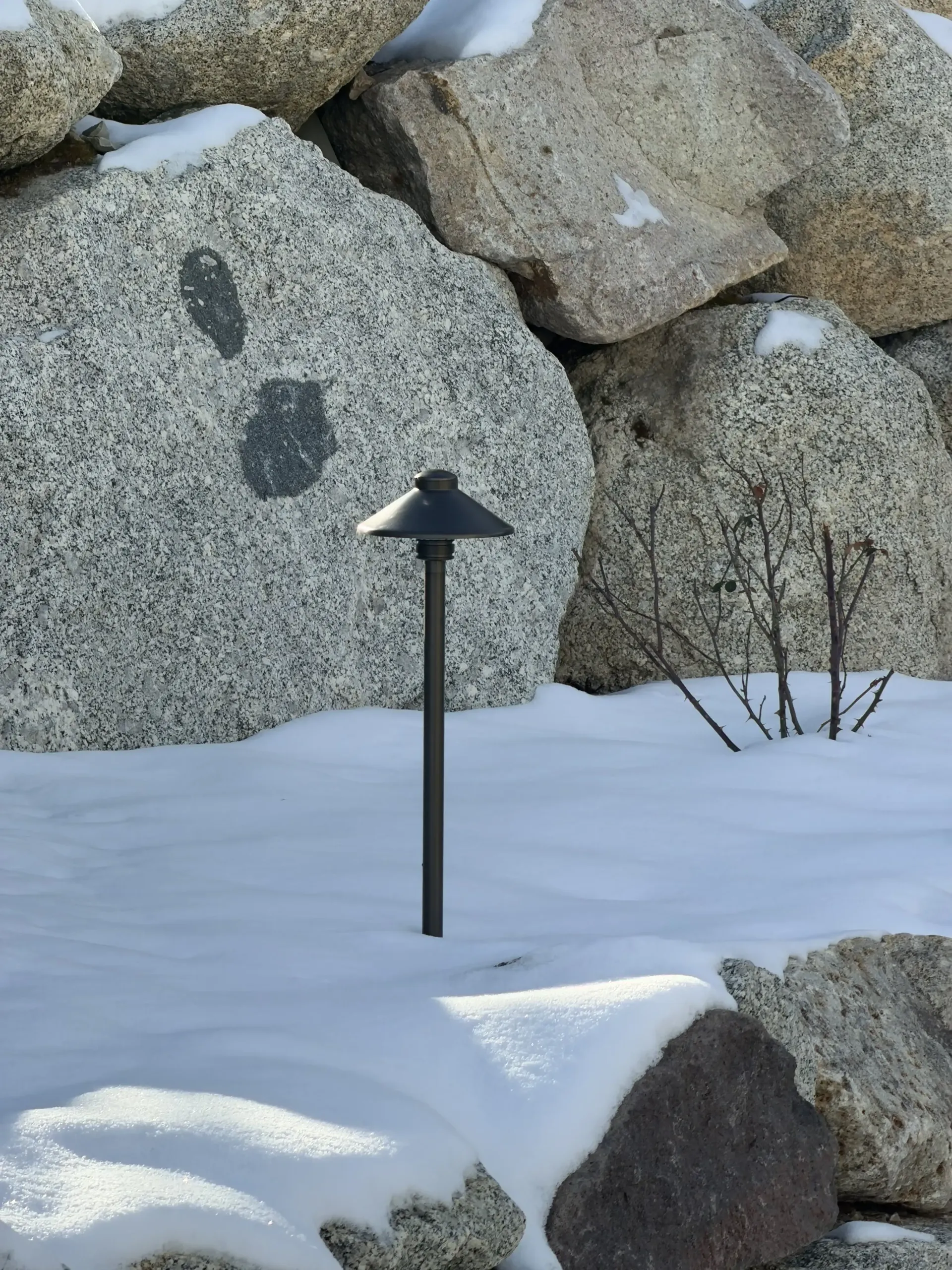 Snow-covered rocks with a black garden light and bare twigs in the foreground Snow-covered rocks with a black garden light and bare twigs in the foreground