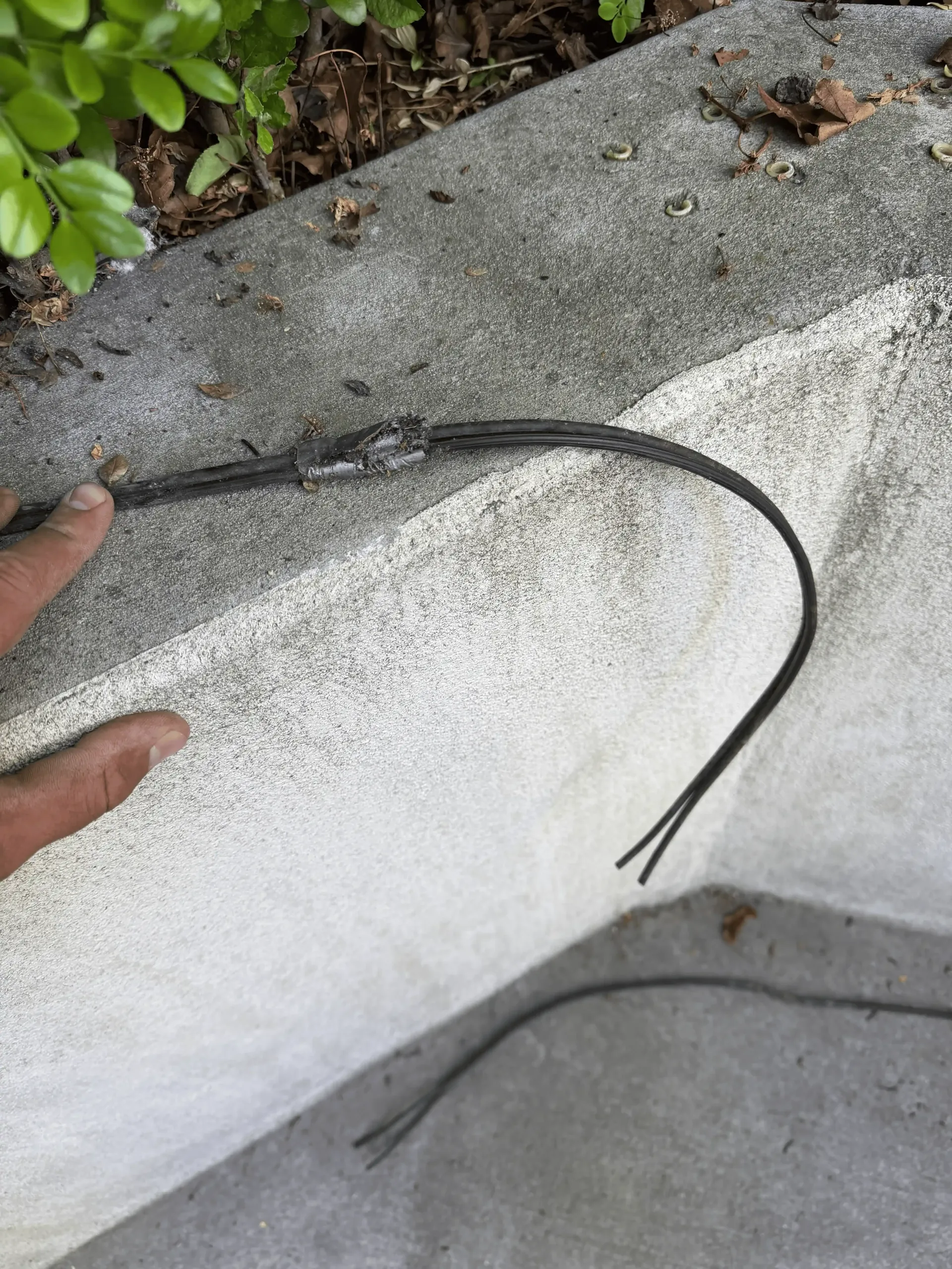 Black cable or wire draped over a white curb, with a hand pointing nearby. Black cable or wire draped over a white curb, with a hand pointing nearby.