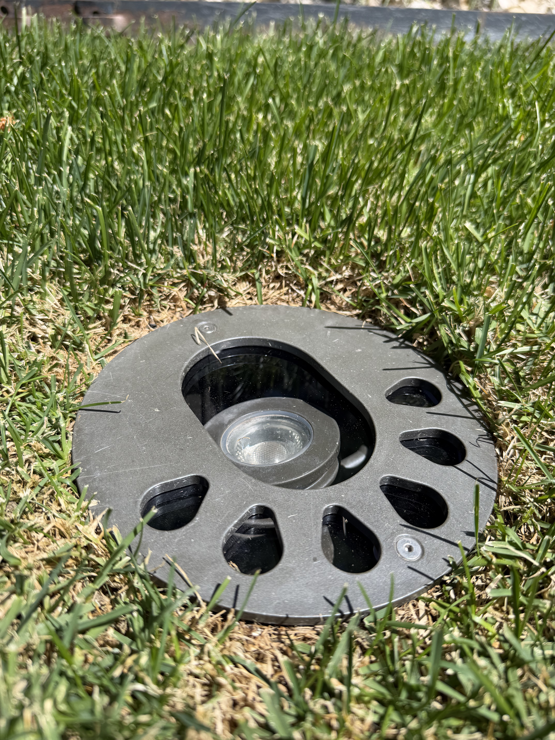 Black landscape light fixture set in green grass, seen close up outdoors. Black landscape light fixture set in green grass, seen close up outdoors.