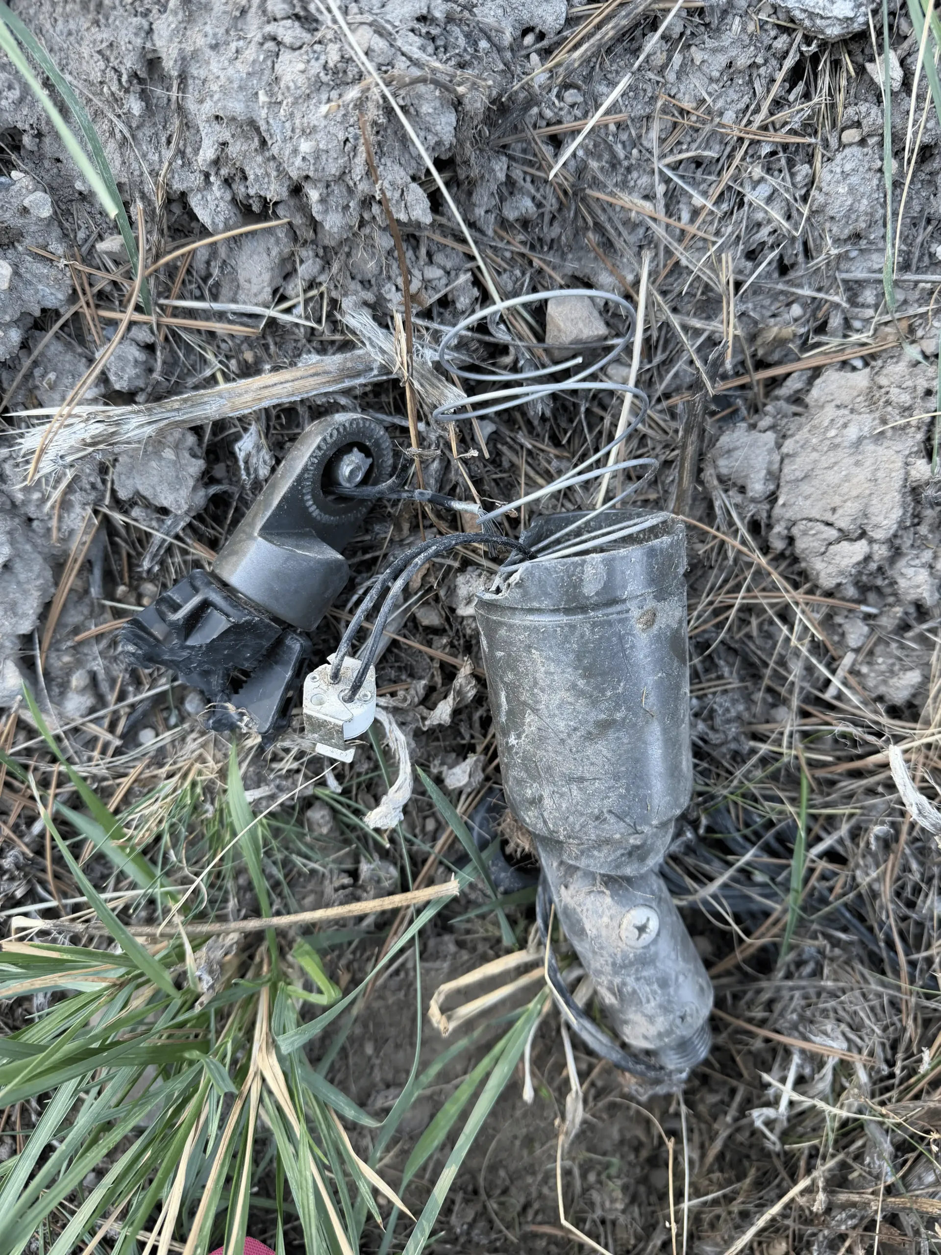 Broken plastic bottle and black mechanical part lying in dirt and grass. Broken plastic bottle and black mechanical part lying in dirt and grass.