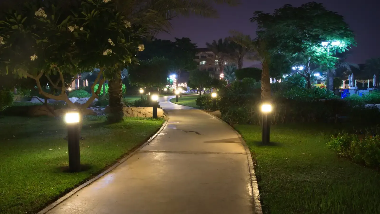 Lit winding park path at night, bordered by grass and glowing lamp posts.