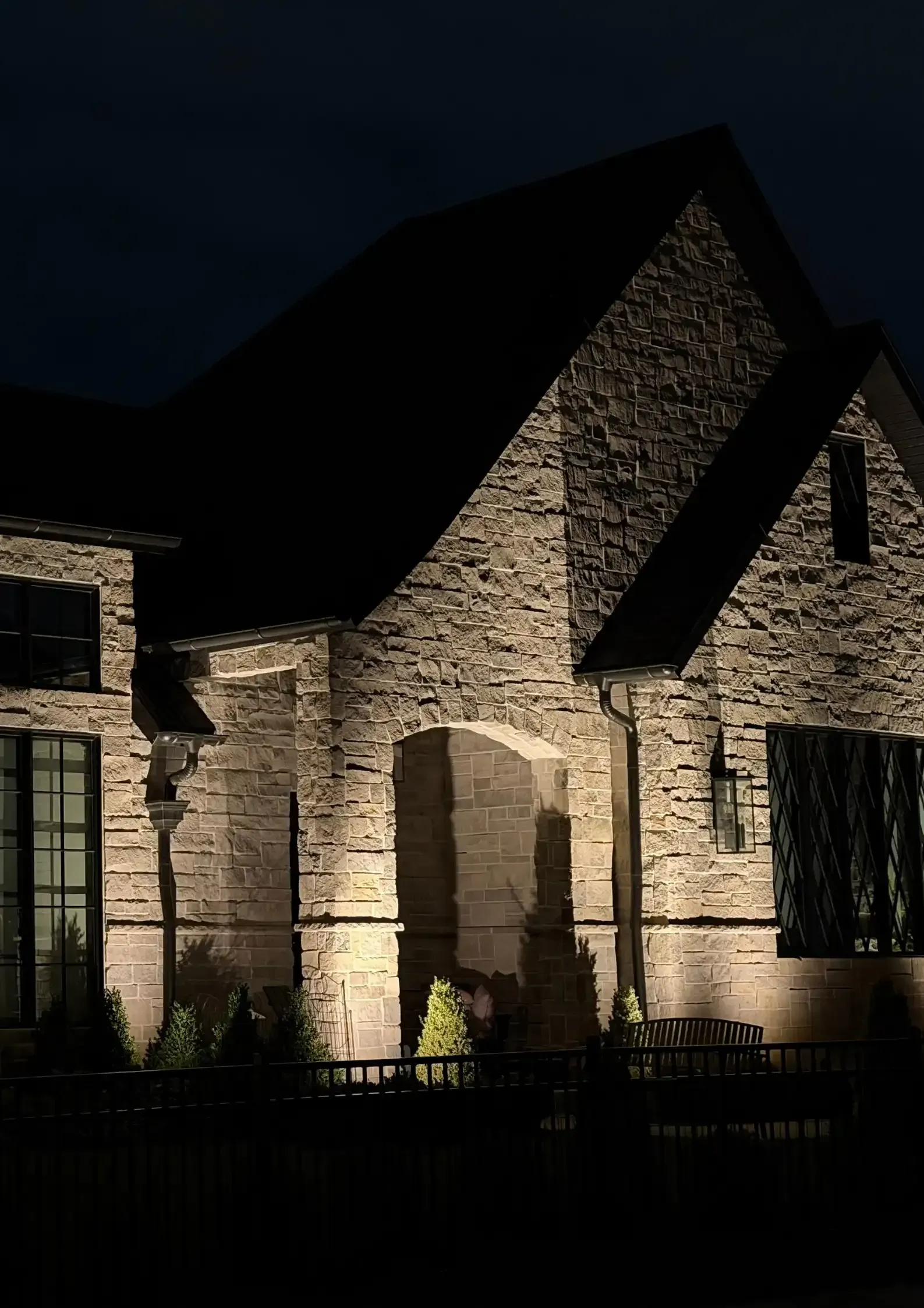 Night-lit stone house facade with arched doorway and dark roof against the night sky Night-lit stone house facade with arched doorway and dark roof against the night sky