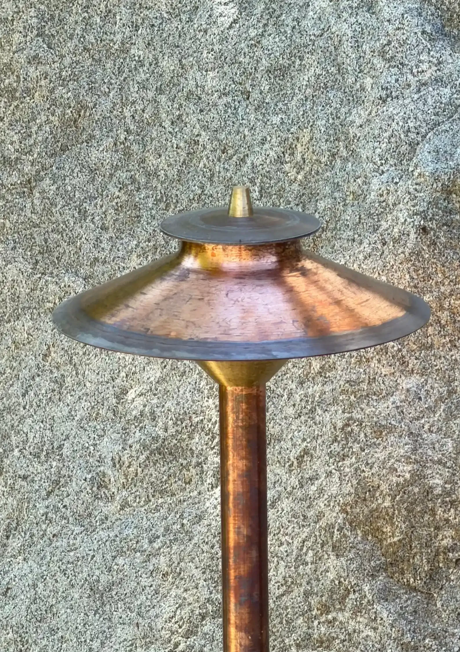 Copper-colored outdoor lamp post with a wide conical shade against a textured stone wall Copper-colored outdoor lamp post with a wide conical shade against a textured stone wall