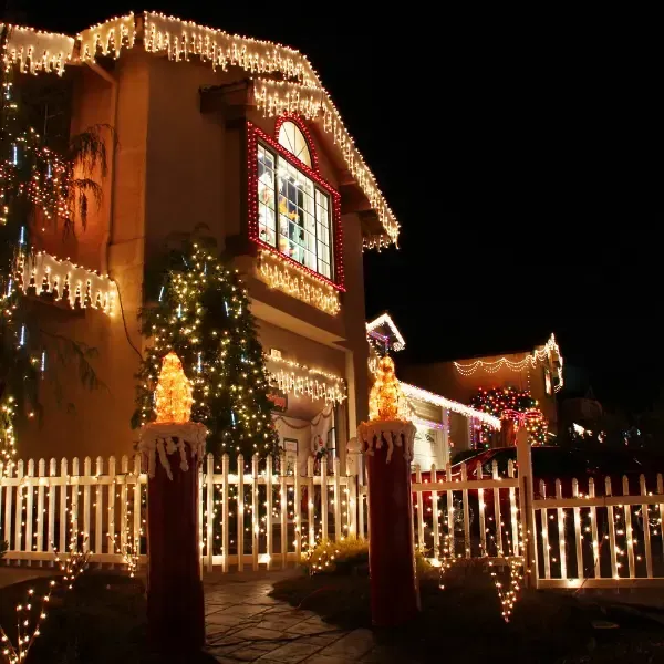 House decorated with warm white Christmas lights and a glowing star, behind a white picket fence at night House decorated with warm white Christmas lights and a glowing star, behind a white picket fence at night